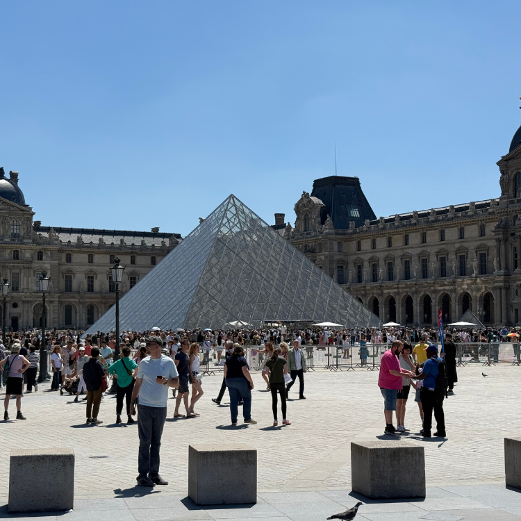 The Louvre Museum courtyard with glass pyramid entrance and many tourists on a sunny day.