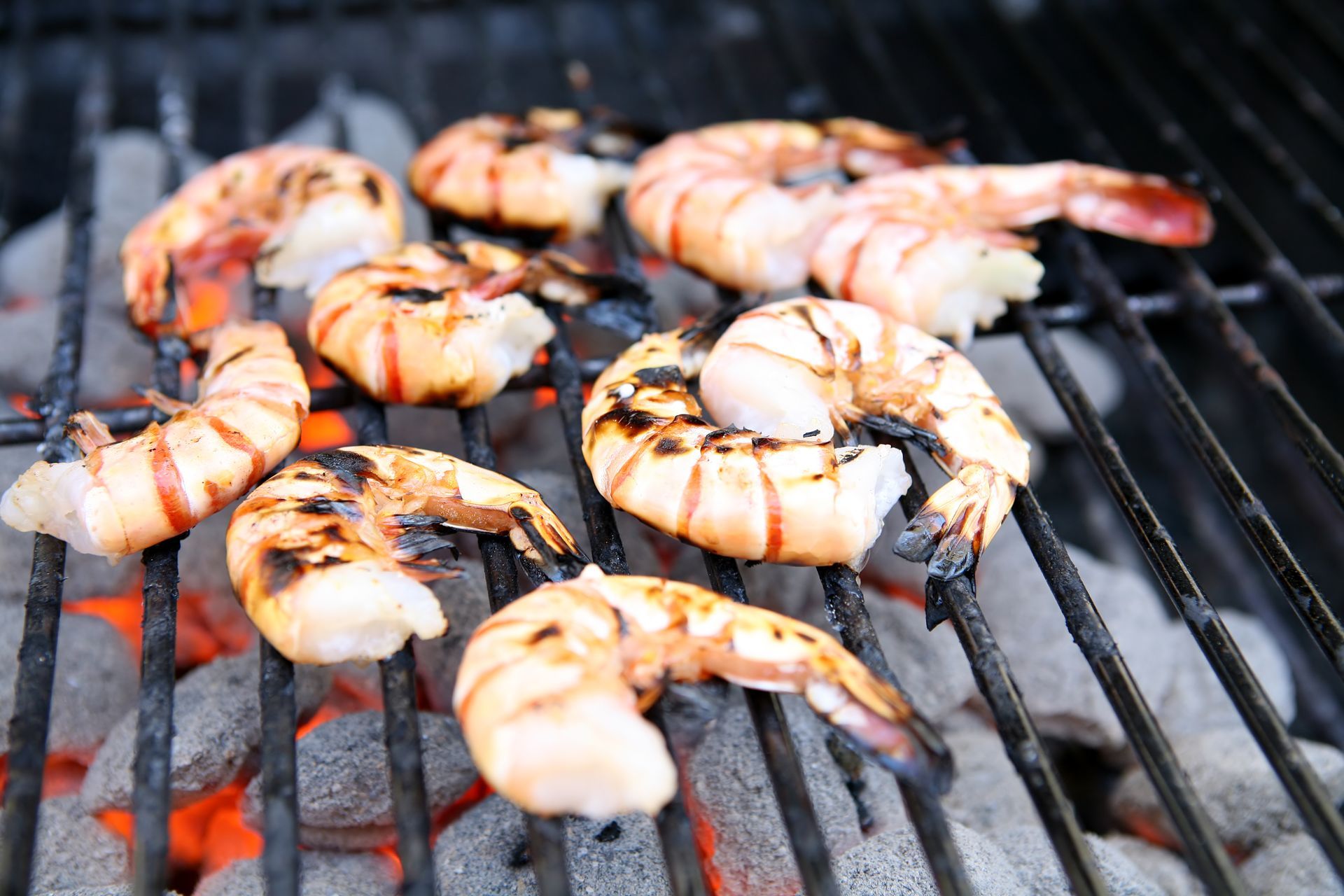 Grilled shrimp on a charcoal grill, showing char marks and bright orange coals.