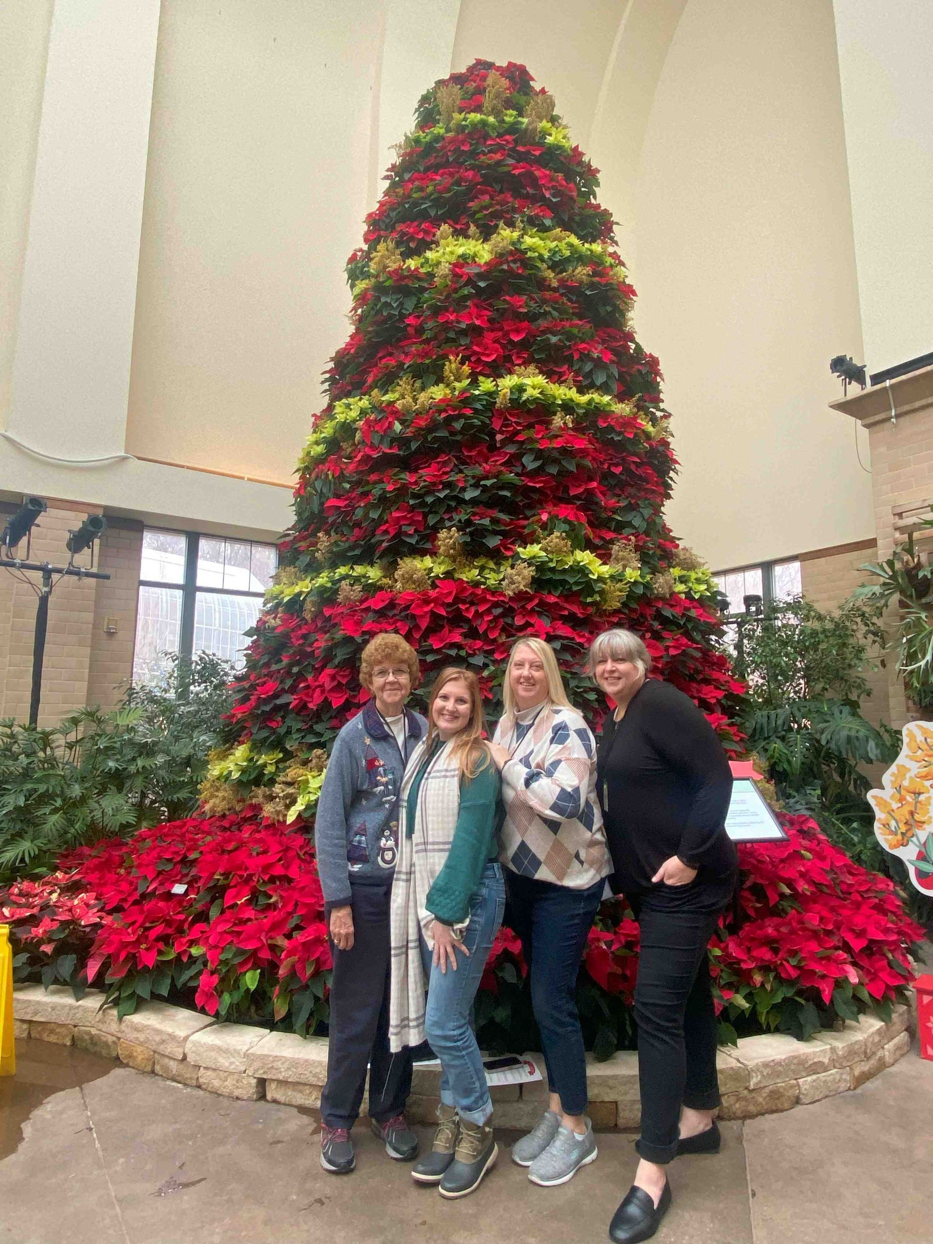A group of women are posing for a picture in front of a christmas tree.