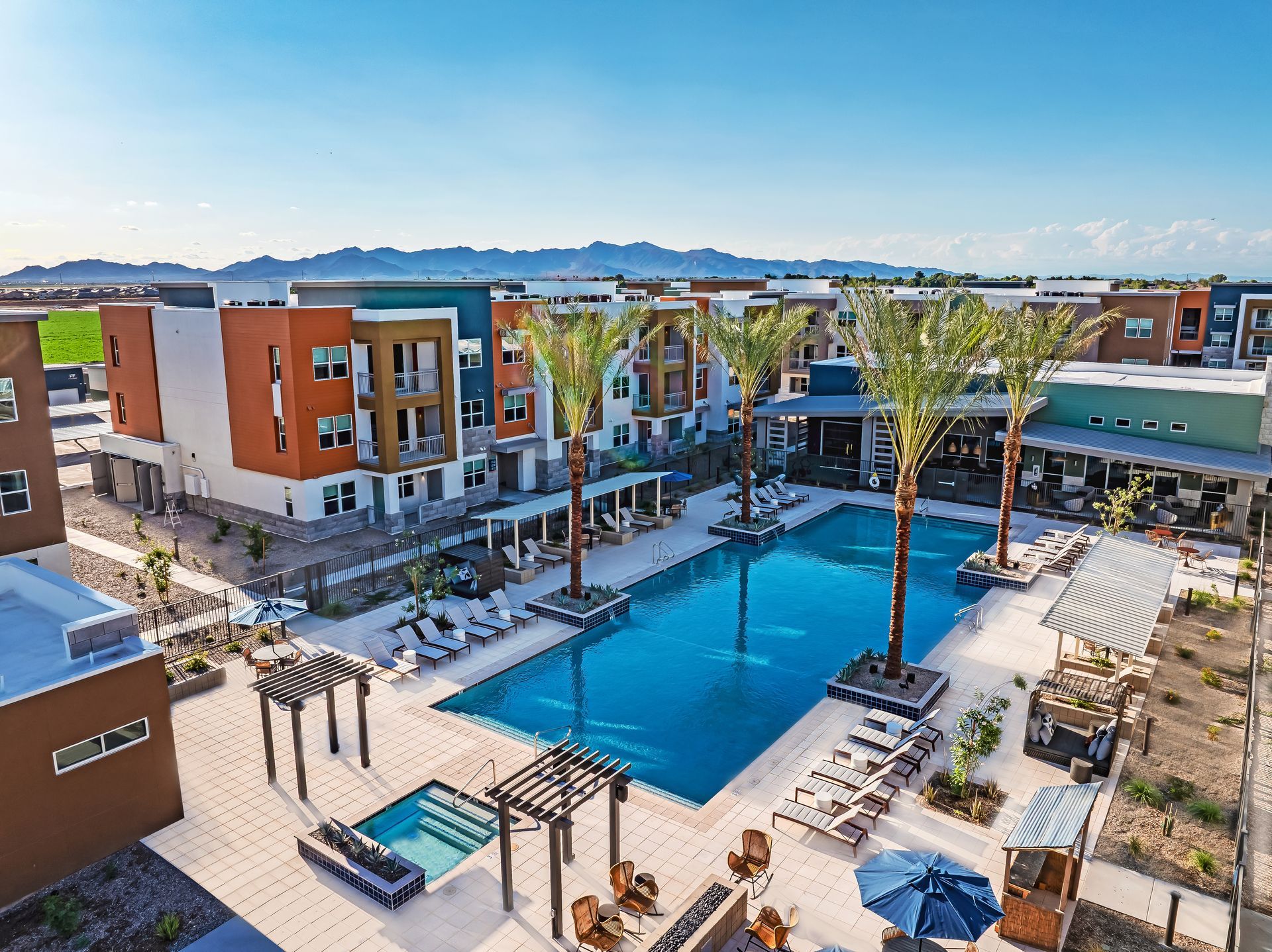 An aerial view of a large swimming pool surrounded by buildings and palm trees at Origin, which offers luxury apartments for rent in Goodyear, AZ.