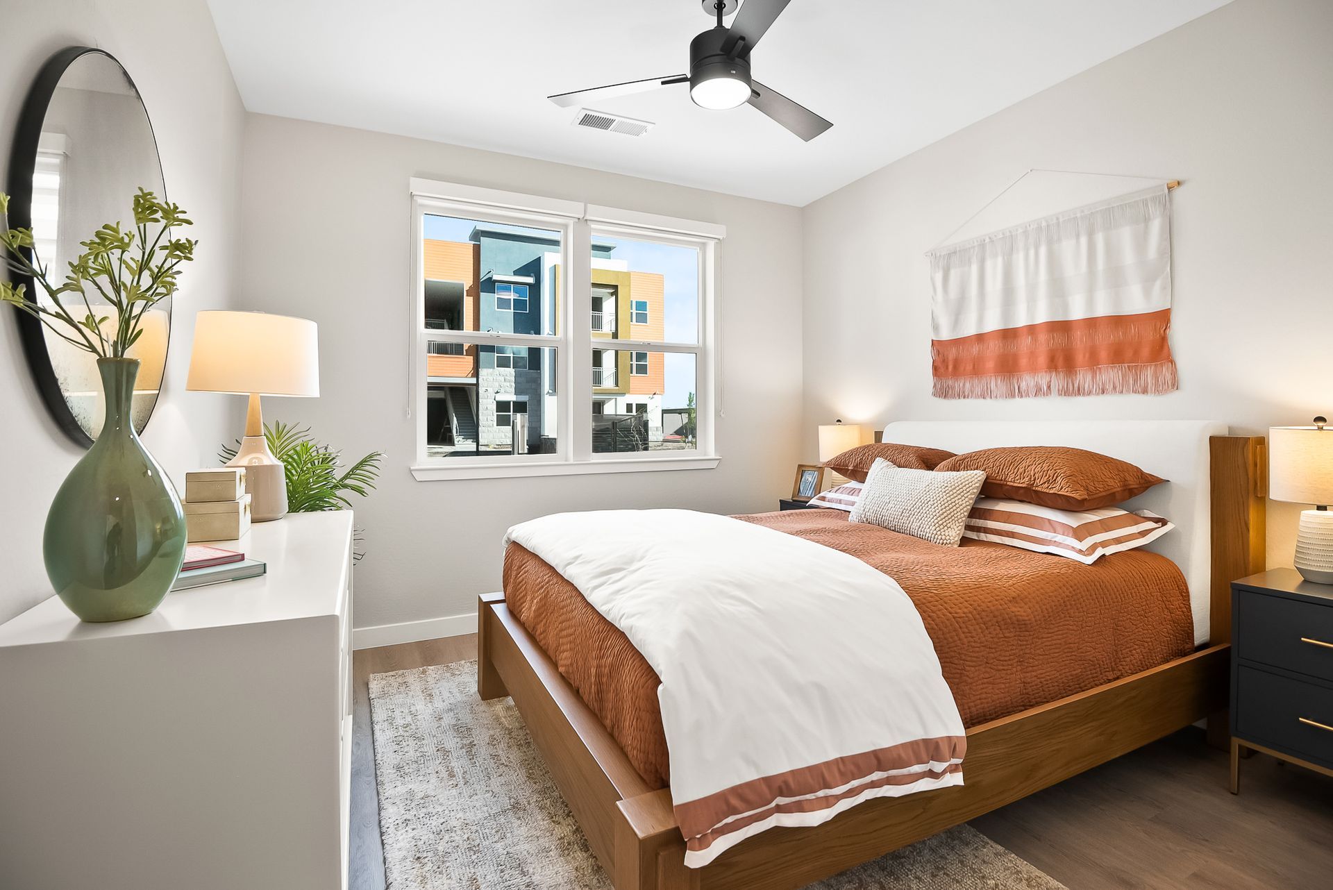 A bedroom with a bed, nightstand, mirror and ceiling fan at Origin, which offers apartments for rent in Goodyear, AZ.