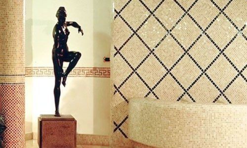 una statua nera di una donna in posa e dei muri piastrellati a mosaico di color beige a linee nere