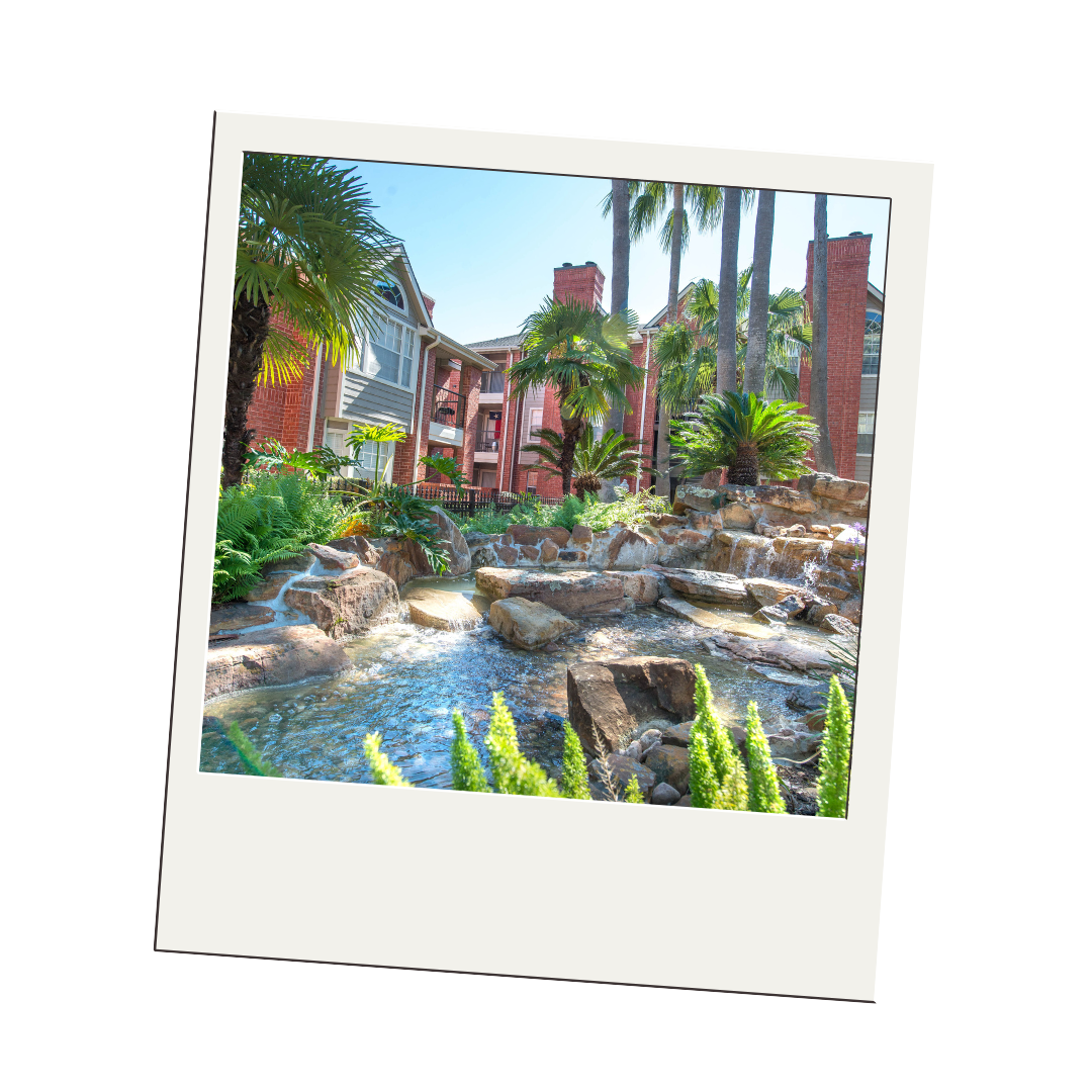 A polaroid picture of a waterfall in a garden with a building in the background.