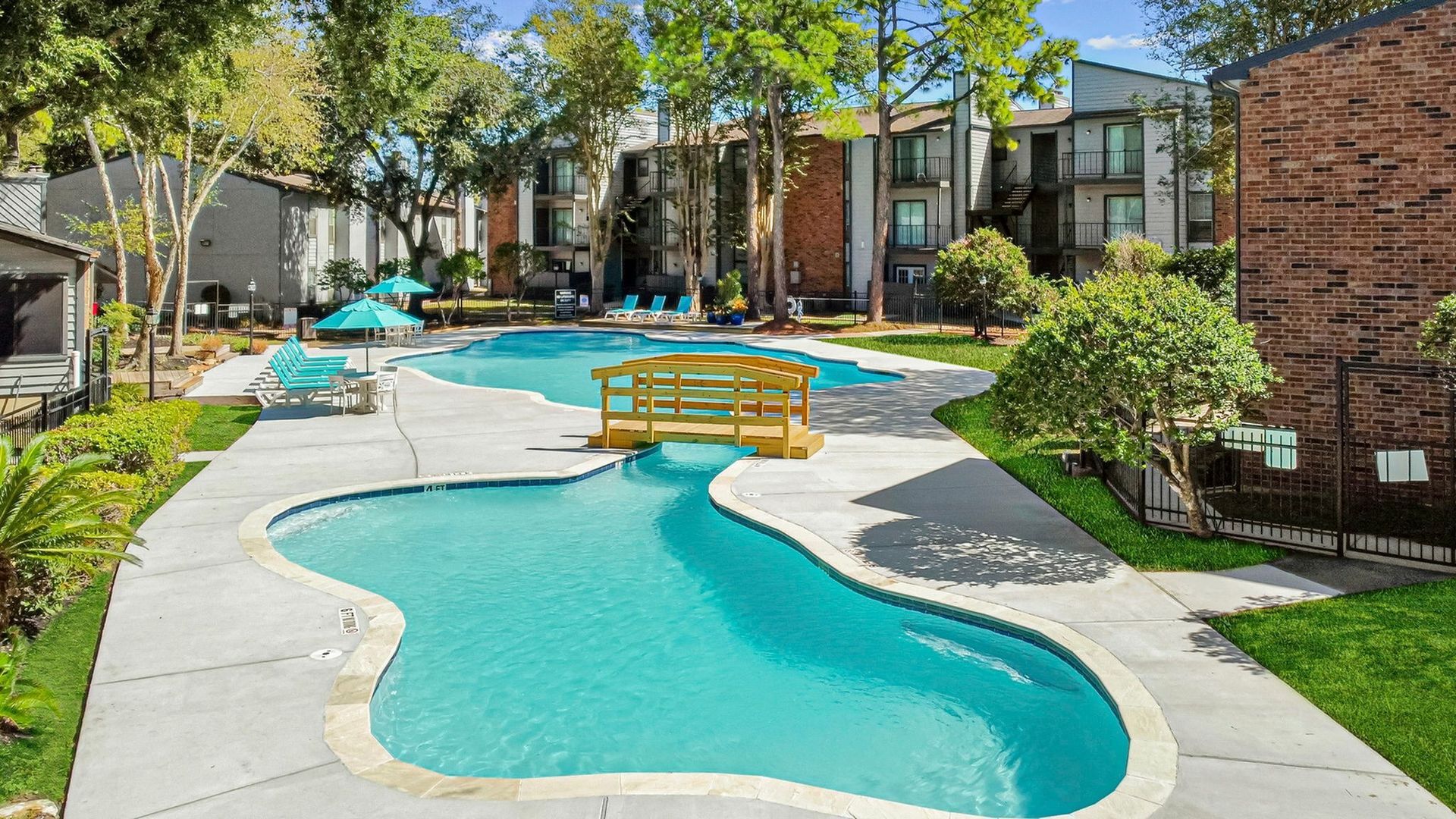 Outdoor communal pool at an apartment complex with lounge chairs and trees.
