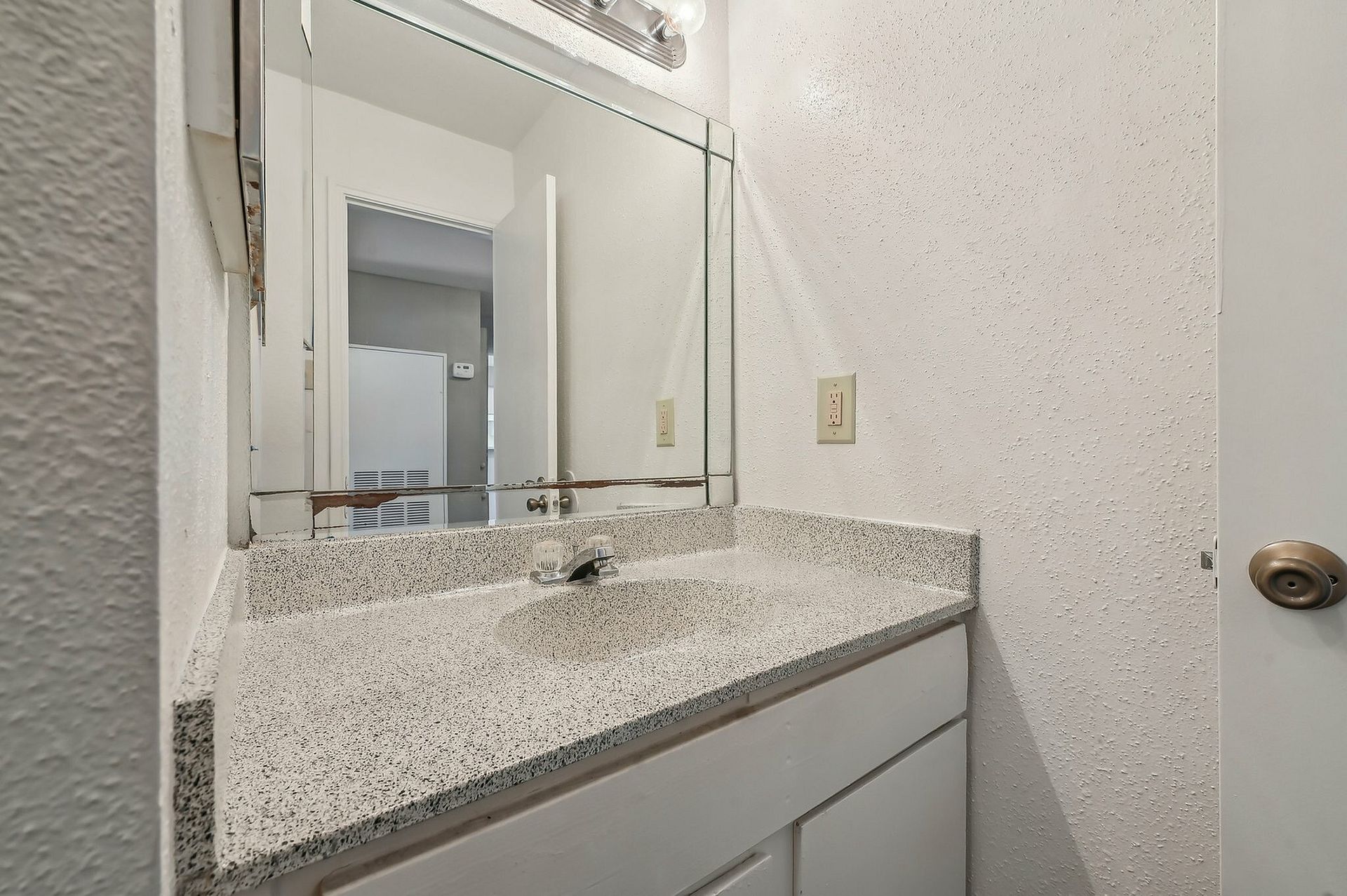 Small bathroom vanity with speckled countertop, sink, and mirrored cabinet.