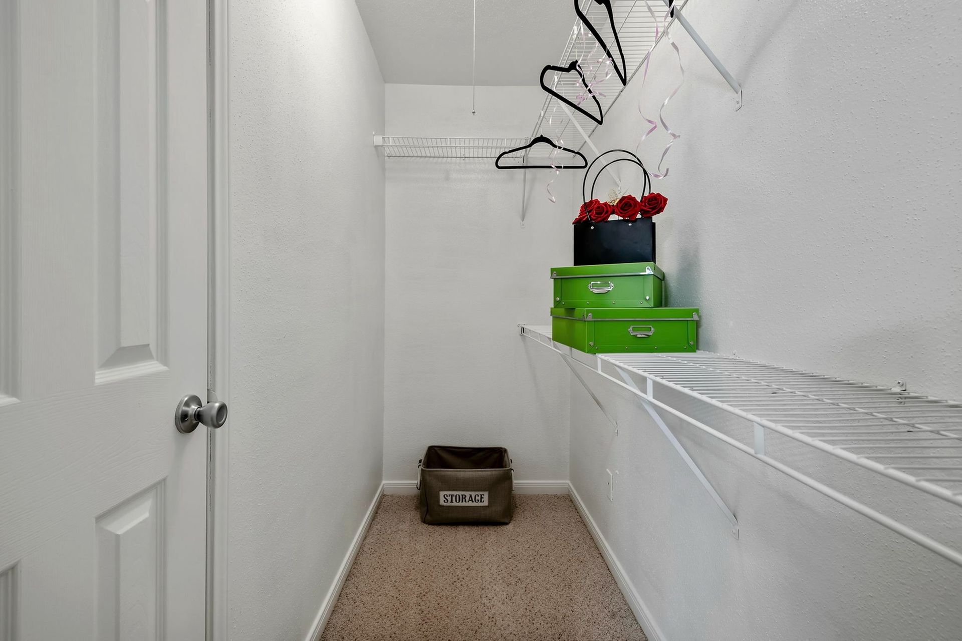 Small walk-in closet with white wire shelves, hanging rods, and storage boxes.