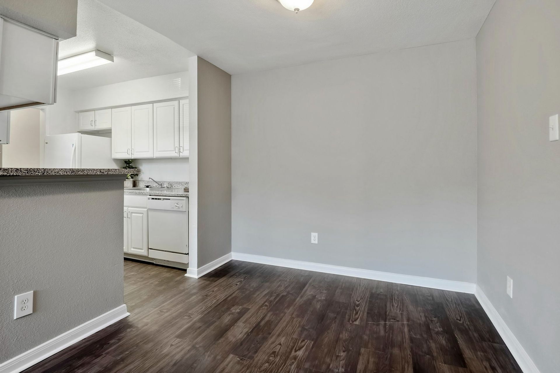 Open-concept living area with white kitchen cabinets and dark wood flooring.