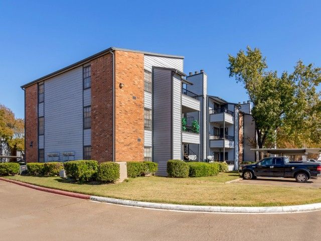 Exterior view of a modern multi-story apartment building with balconies and neatly trimmed shrubs.