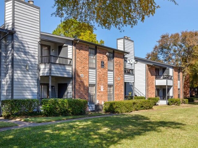 Exterior view of a two-story apartment building with brick and siding, balconies, and a green lawn.