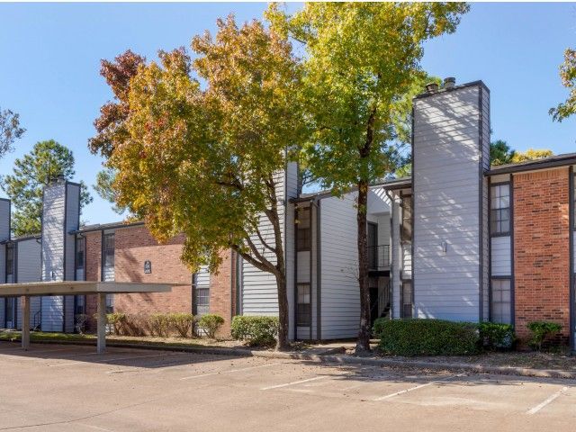 Exterior view of a multi-building apartment complex with trees and a parking lot.
