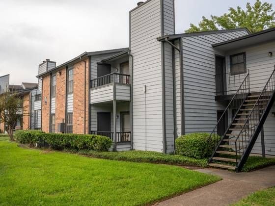 Exterior view of a multi-building apartment complex with balconies and a green lawn.