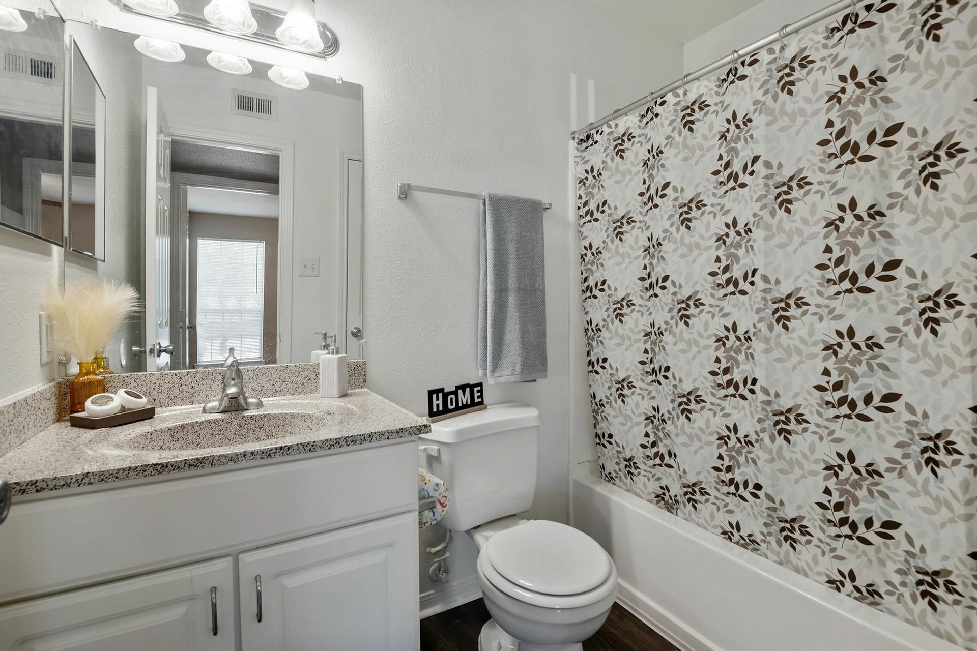 Bathroom with a granite countertop vanity, mirror, toilet, and a floral shower curtain.