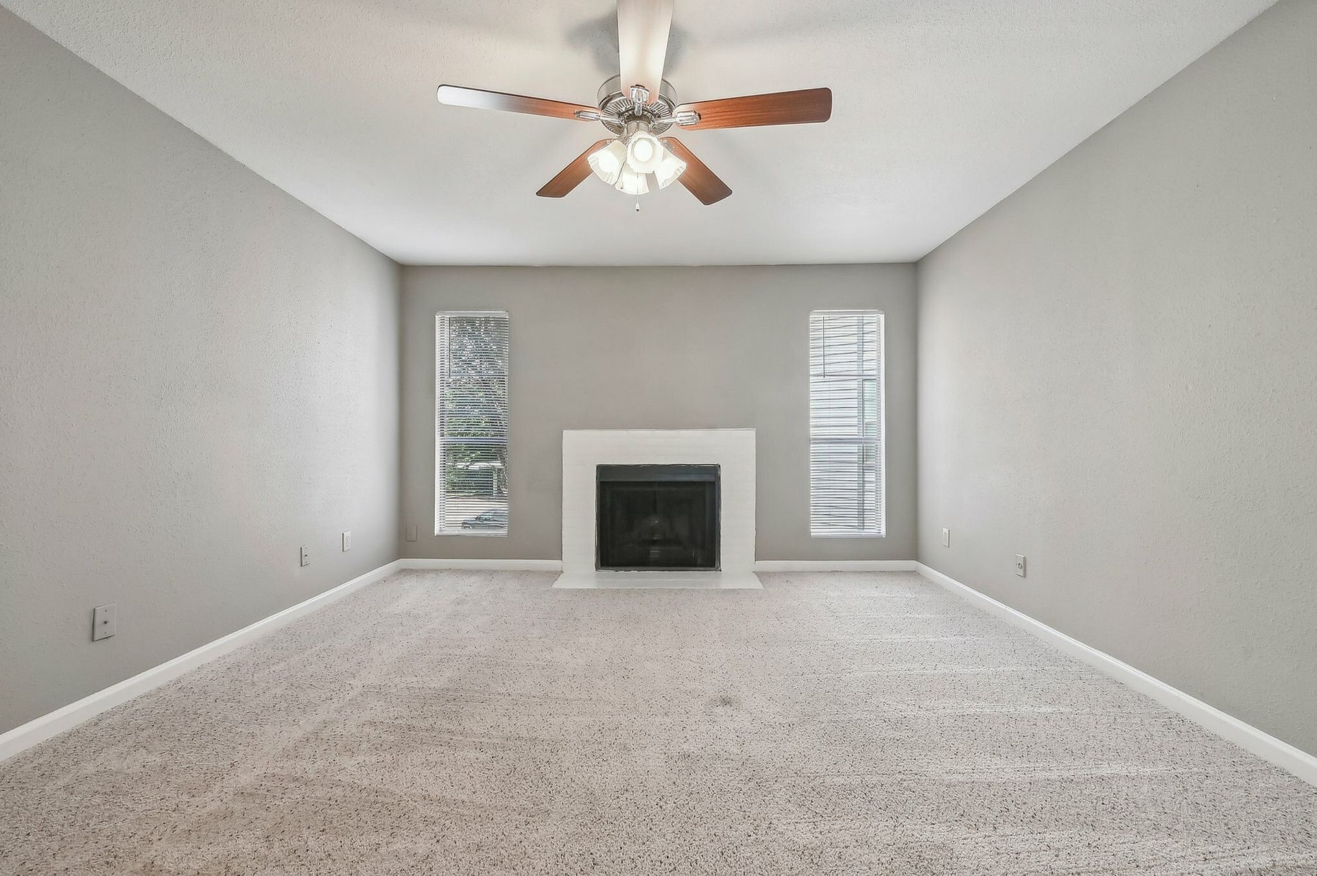 Living room with gray walls, beige carpet, a ceiling fan, and a fireplace between two narrow windows.