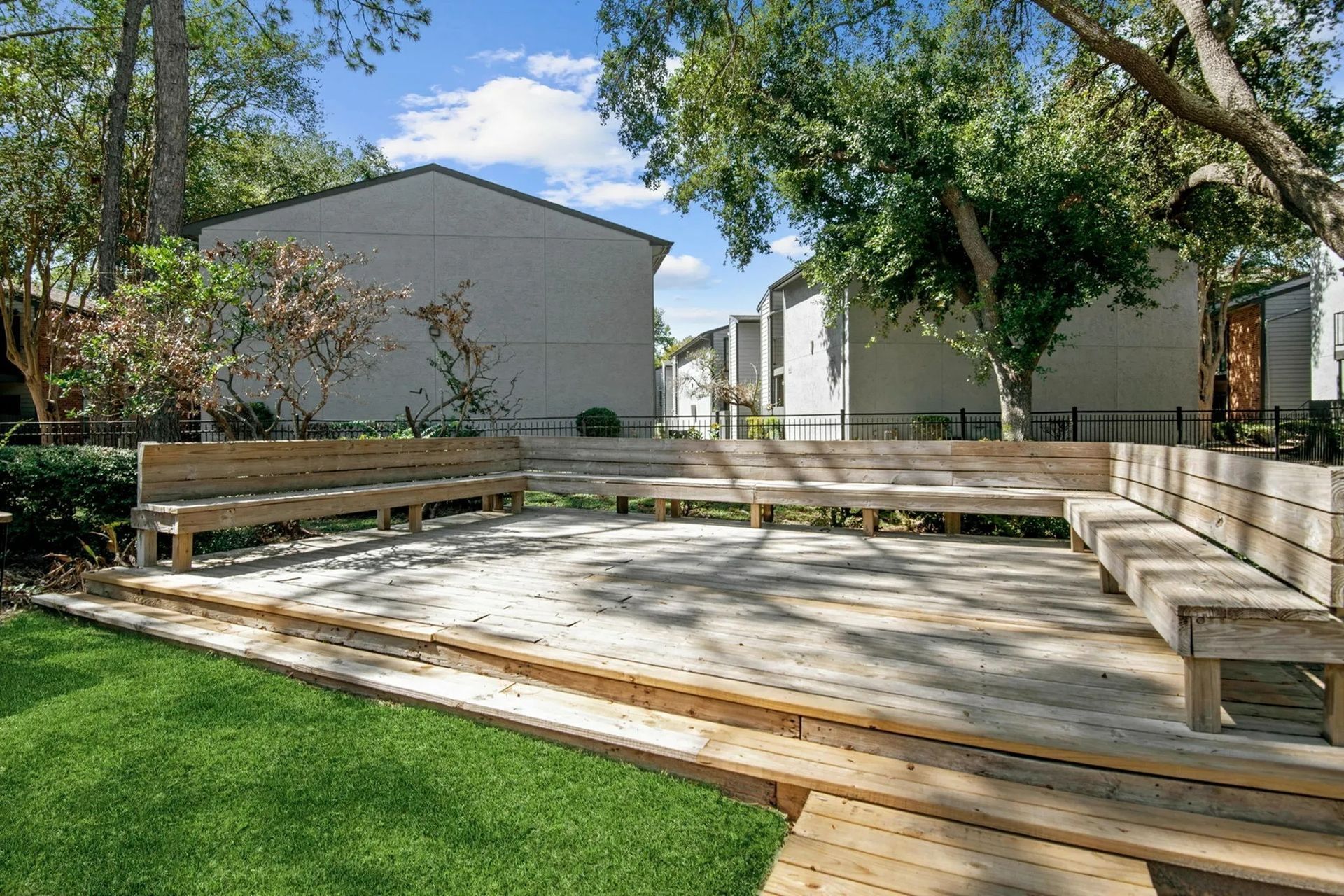 Wooden benches on a deck overlook a lawn, with apartment buildings in the background at Driscoll Place in Houston, TX.