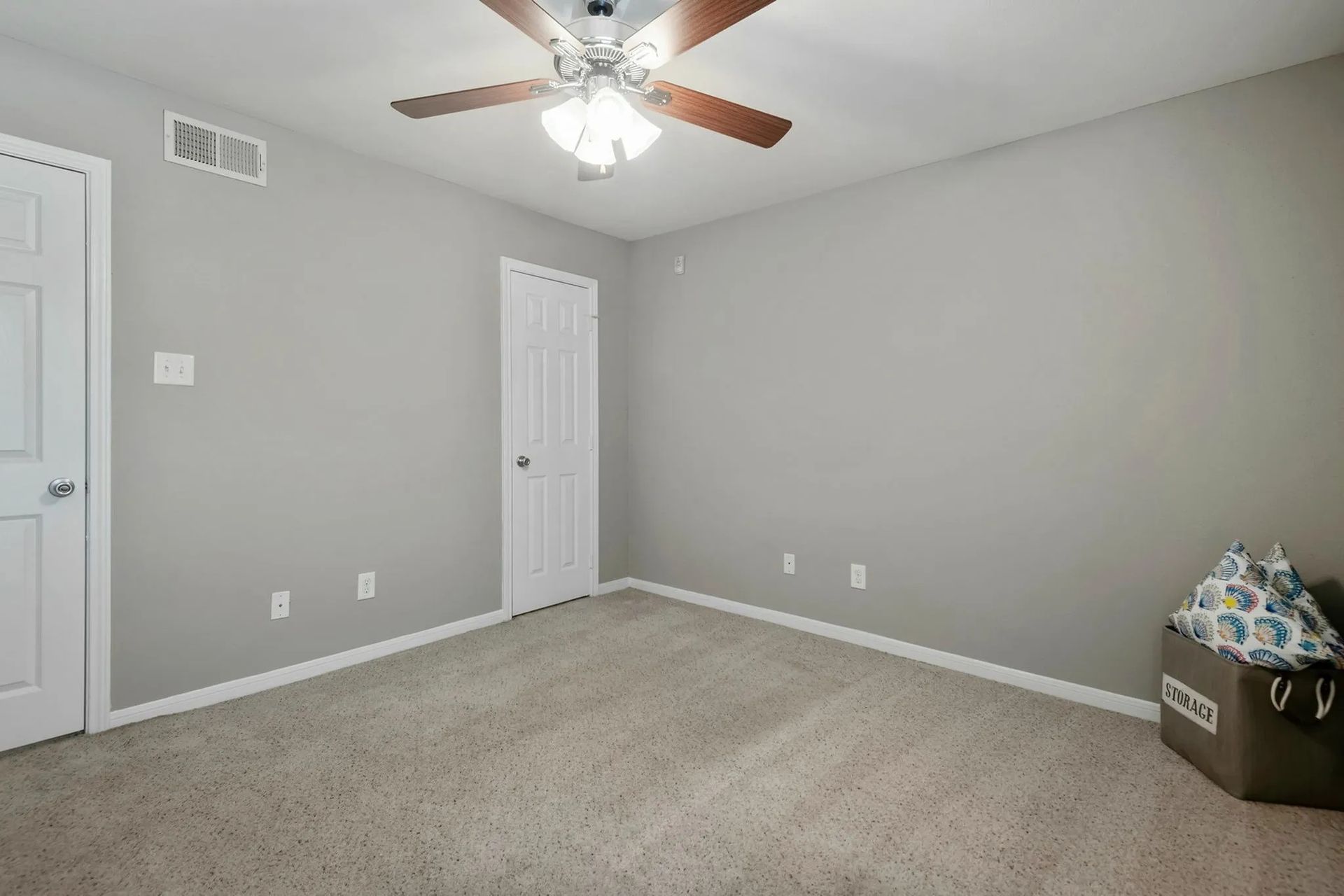 Empty bedroom with gray walls, white trim and doors, ceiling fan, carpet, and a toy chest at Driscoll Place in Houston, TX.