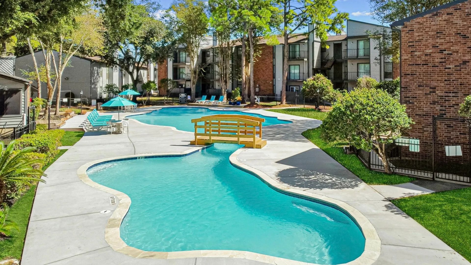 Swimming pool at apartment complex with a small wooden bridge over the water at Driscoll Place in Houston, TX.