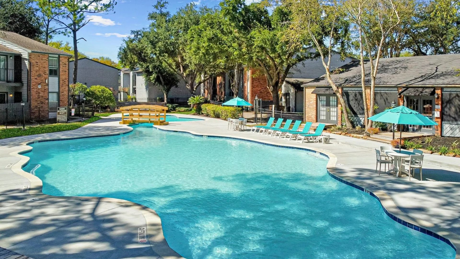 Swimming pool with turquoise water and lounge chairs, near apartment buildings, trees, and umbrellas at Driscoll Place in Houston, TX.