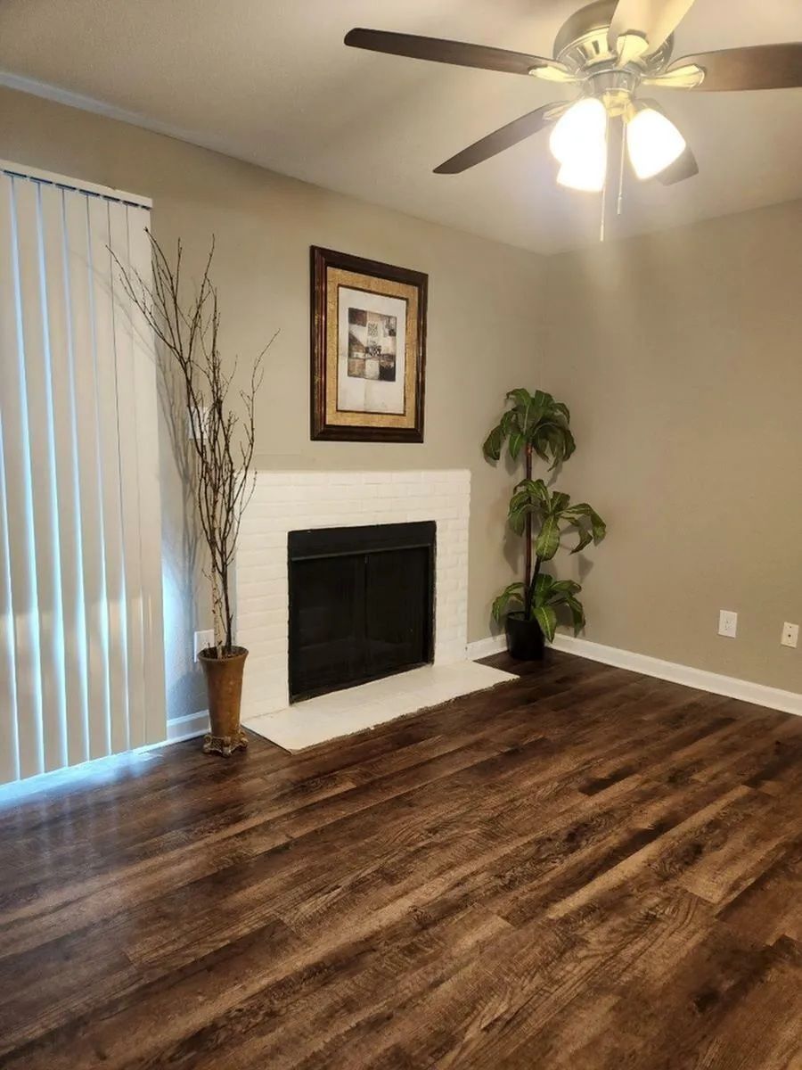 Living room with fireplace, dark wood floor, beige walls, white trim, tall decor, and a ceiling fan at Driscoll Place in Houston, TX.