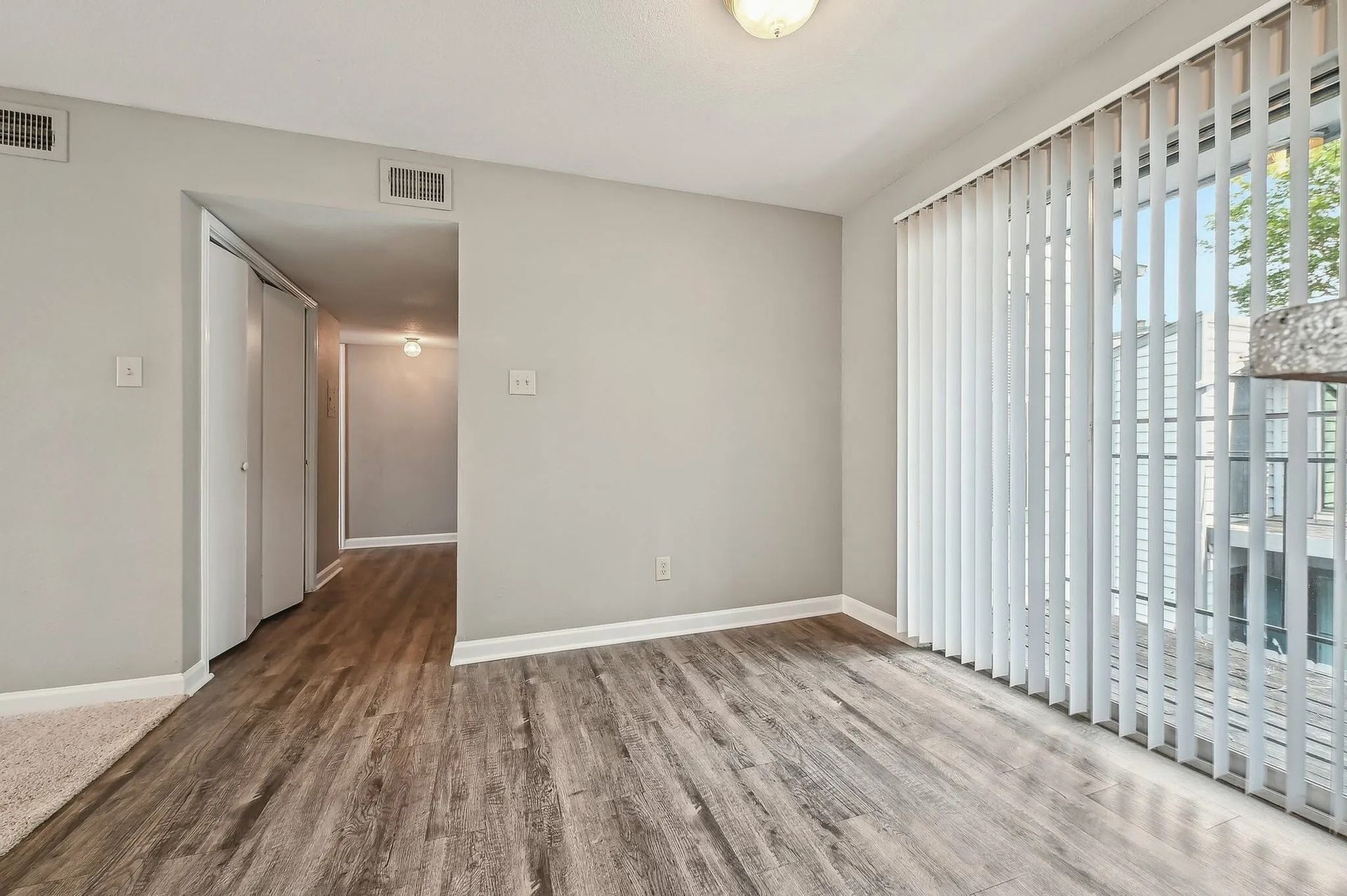 Empty room with wood-look floors, gray walls, vertical blinds, and a hallway leading to other rooms at Driscoll Place in Houston, TX.