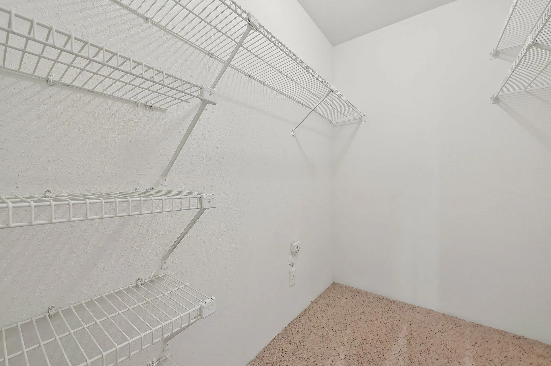 Empty white wire shelving inside a small walk-in closet, with a speckled beige floor at Driscoll Place in Houston, TX.
