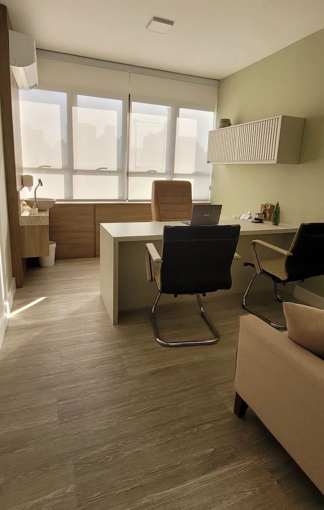 Escritório moderno com mesa, cadeiras e grandes janelas com persianas. Madeira clara e tons neutros.