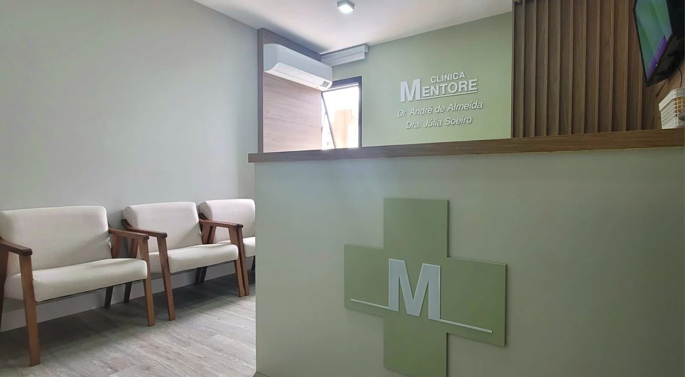 Área de recepção com paredes verde-claras, cadeiras e balcão com o logotipo da cruz médica.