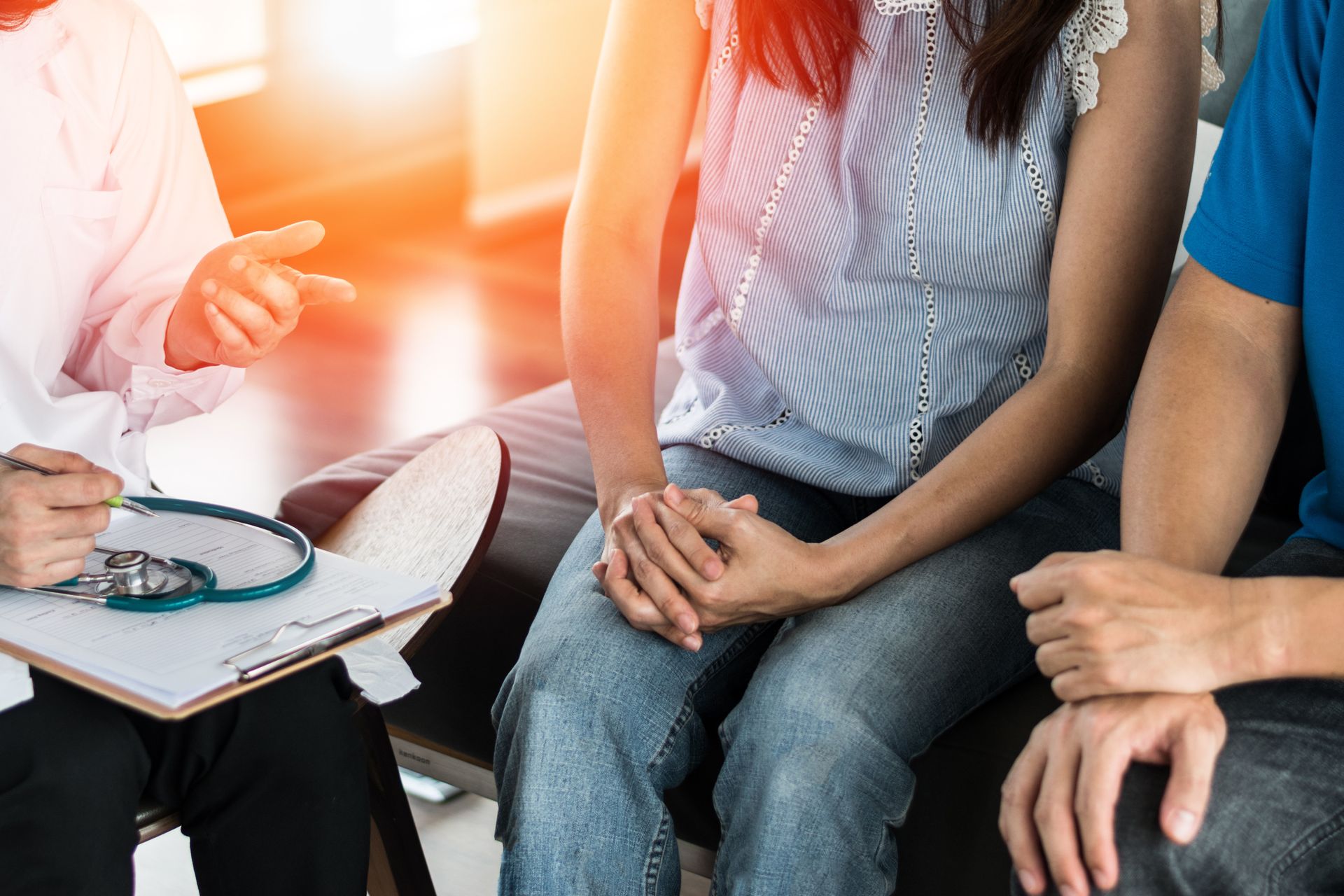 Médico conversando com um casal em um consultório. A mulher e o homem estão sentados; luz solar.