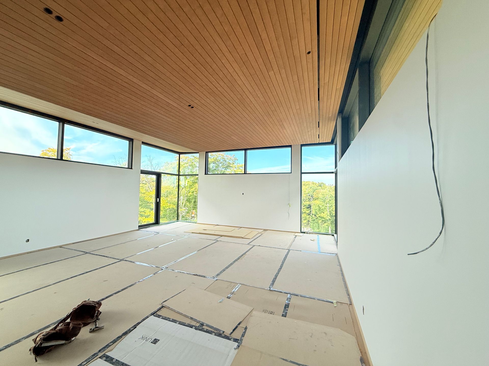 Intérieur d'une pièce en construction avec un plafond en bois, de grandes fenêtres et des murs blancs inachevés.