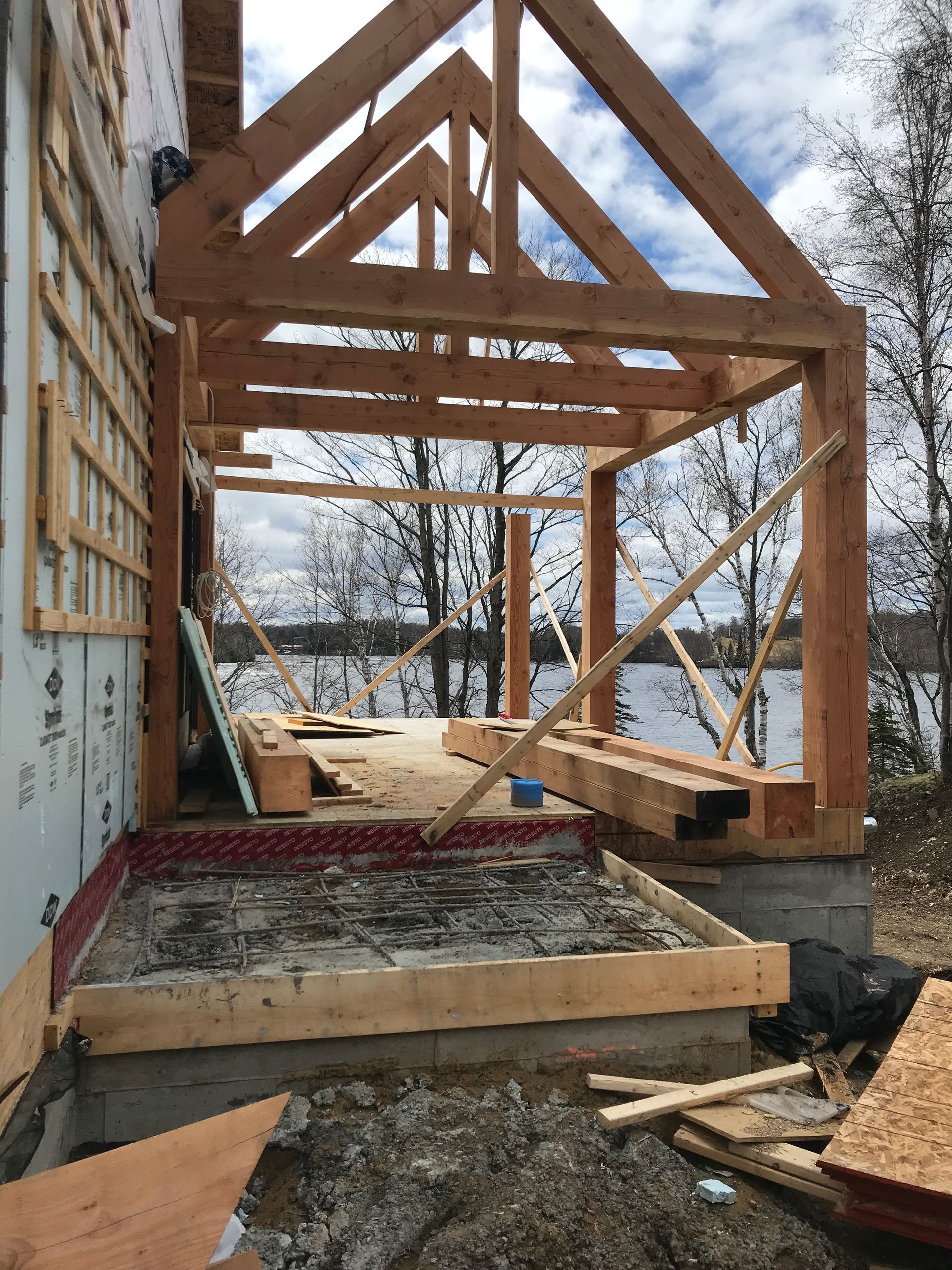 Véranda en bois en construction, avec un lac en arrière-plan.