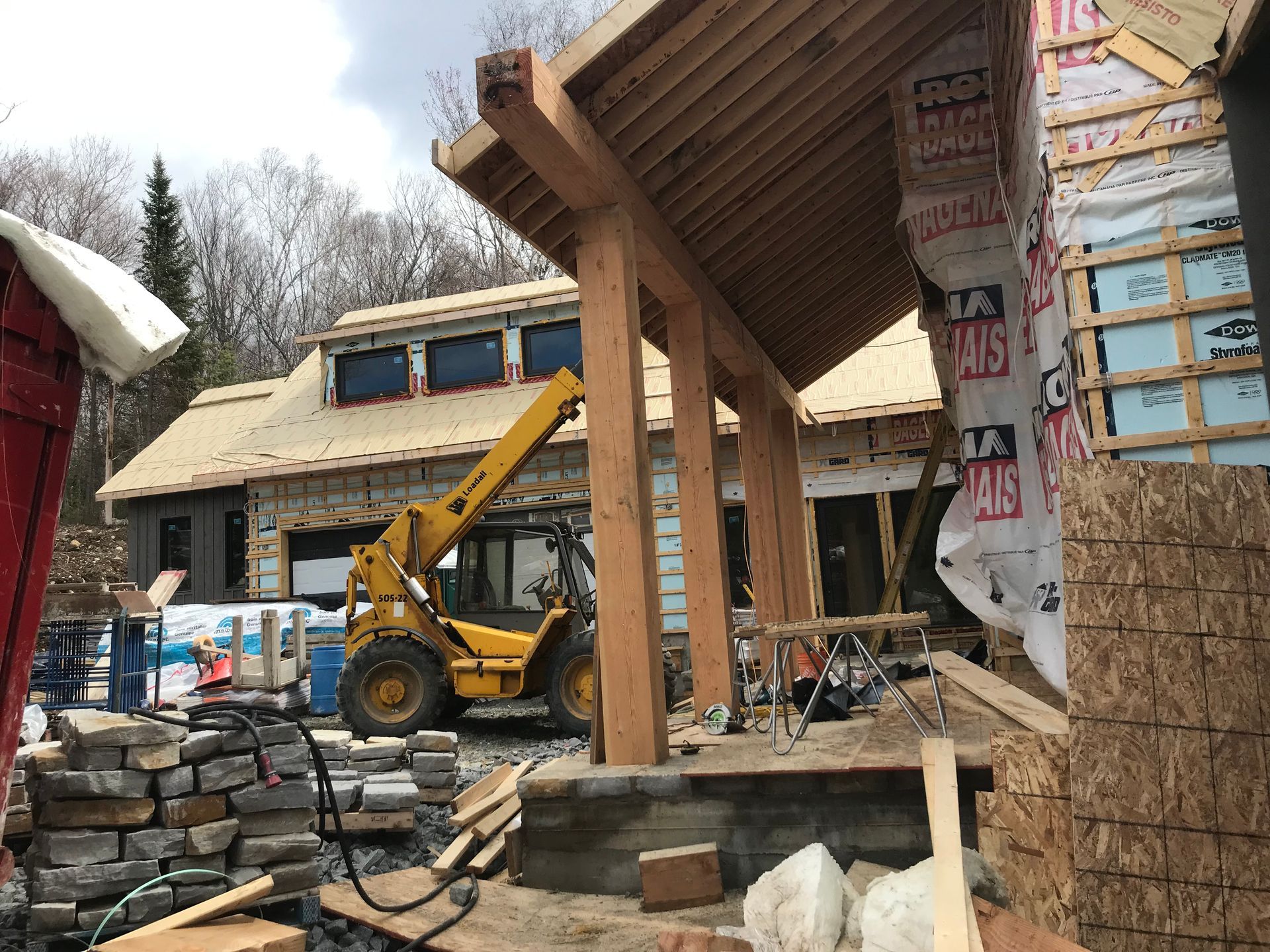 Construction d'une maison avec des poutres en bois, un chariot élévateur jaune et des matériaux de construction.