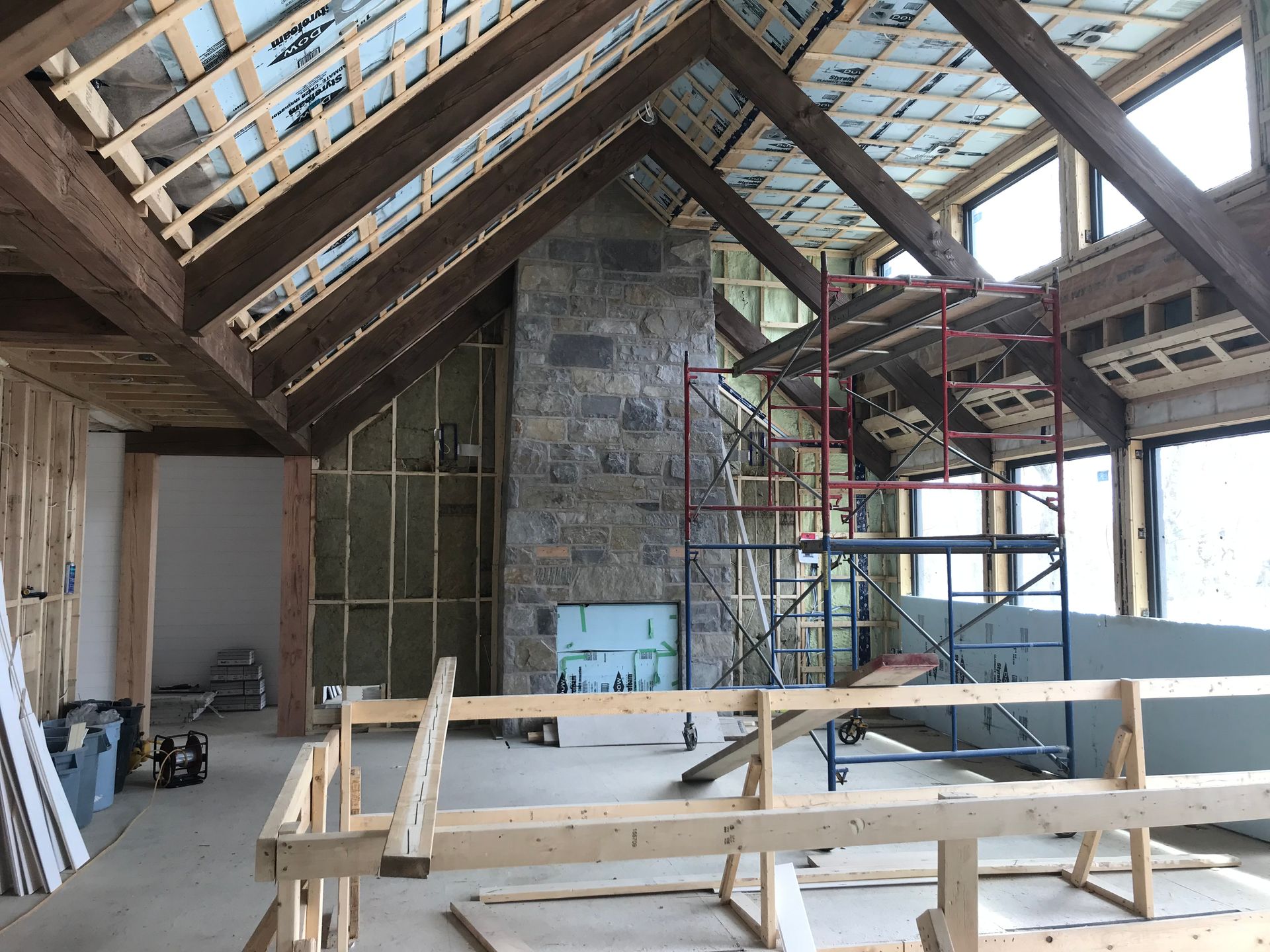 Intérieur d'un bâtiment en construction, montrant des poutres en bois apparentes, une cheminée en pierre et des échafaudages.