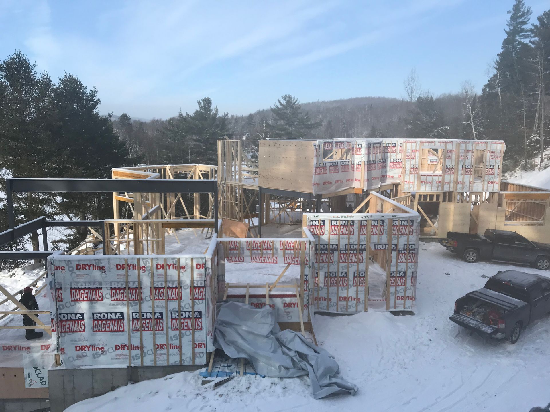 Chantier de construction d'une maison en hiver ; charpente en bois, isolation, neige et véhicules.