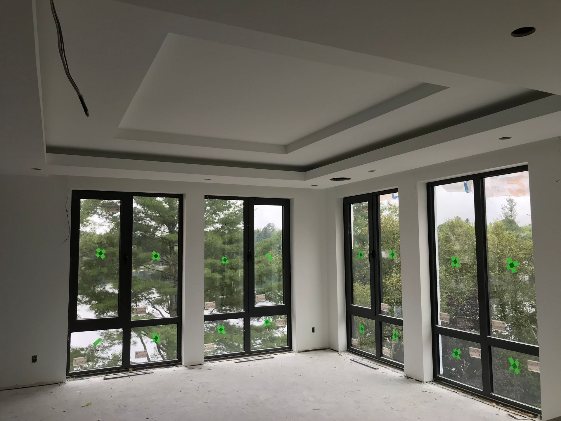 Pièce intérieure avec de grandes fenêtres, construction inachevée, plafond en retrait, vue sur les arbres.
