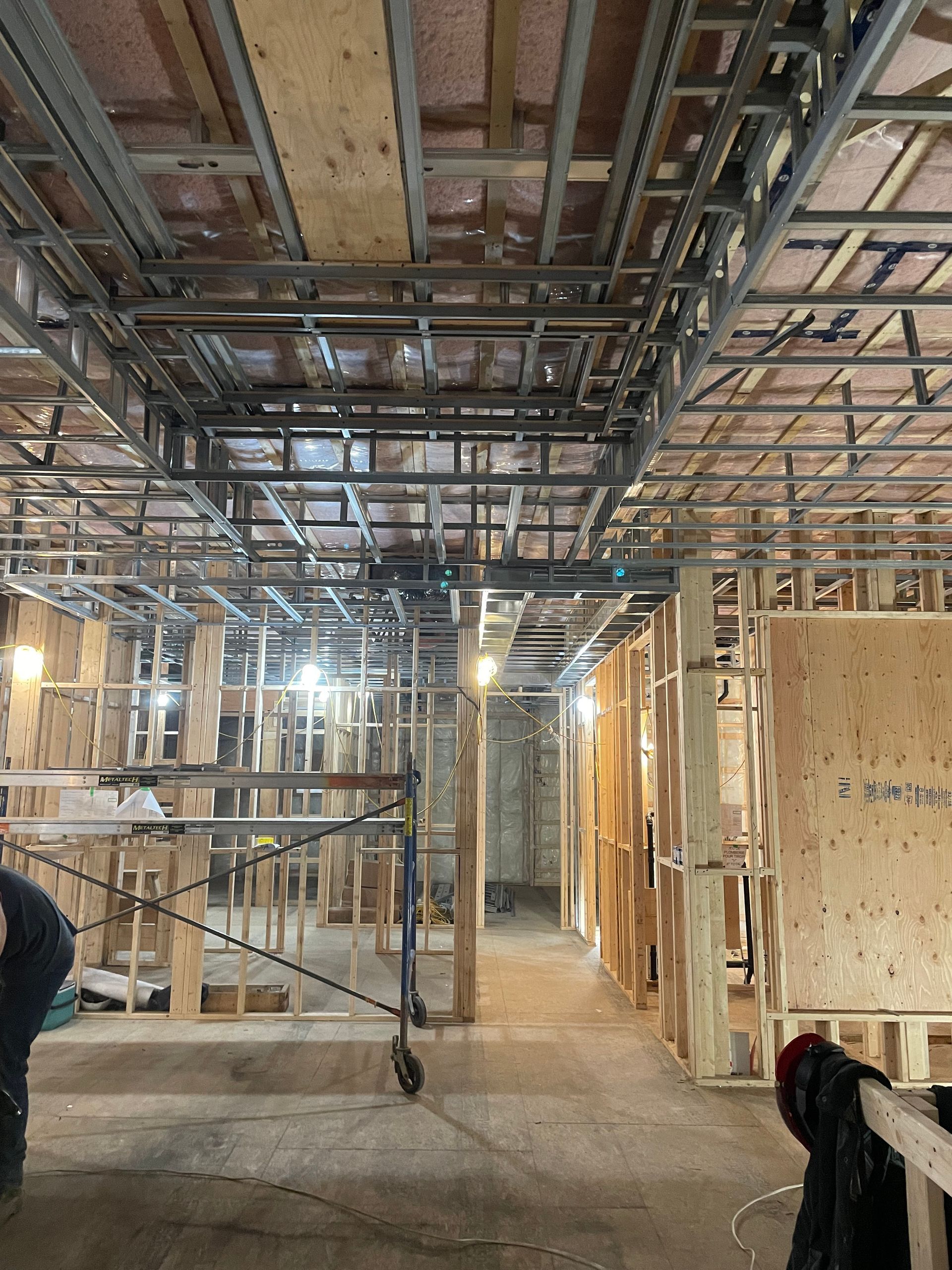 Vue intérieure d'un bâtiment en construction, montrant la charpente, la grille de plafond et les échafaudages.