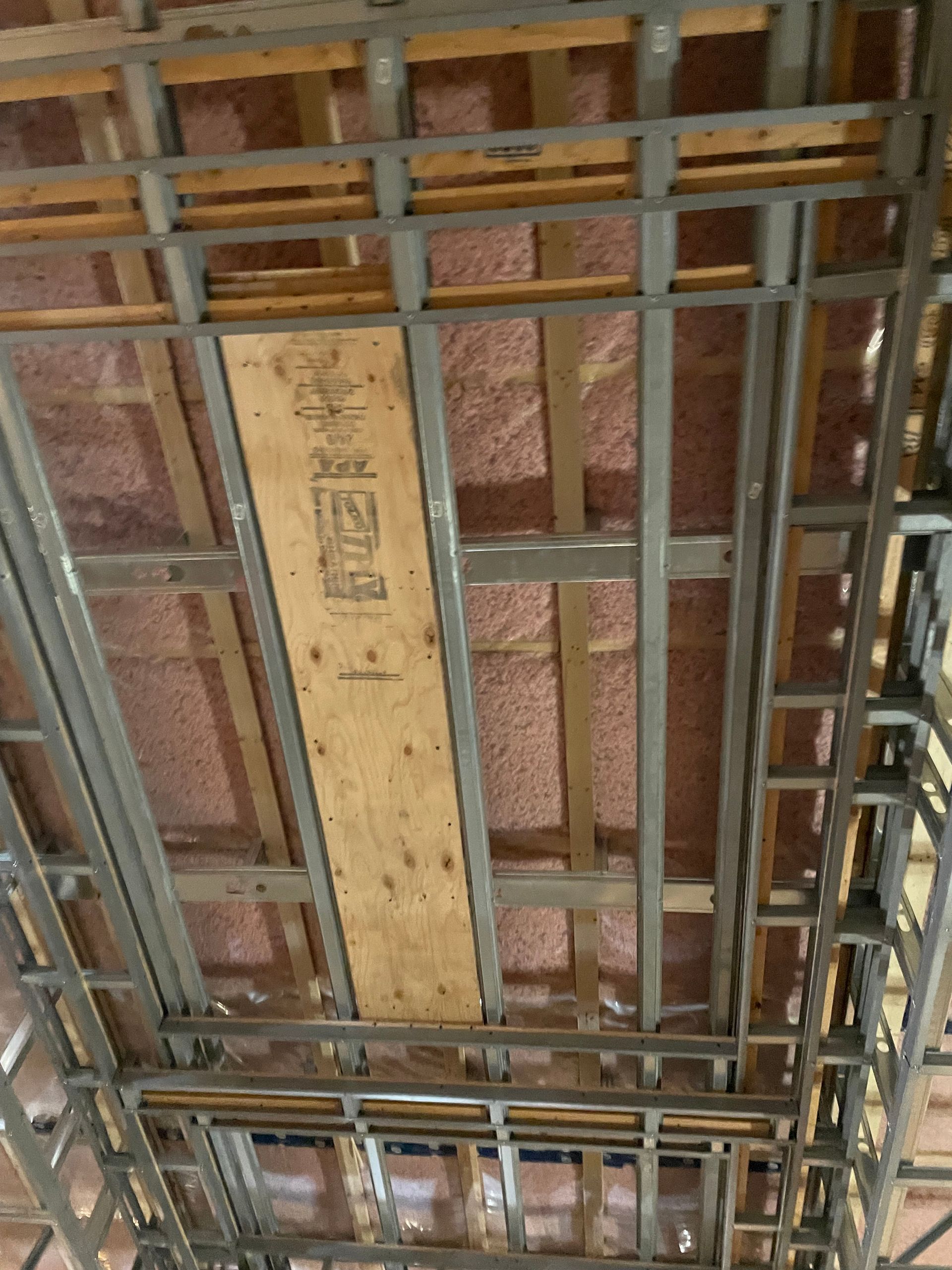 Ossature métallique et en bois d'un plafond laissant apparaître l'isolant rose.