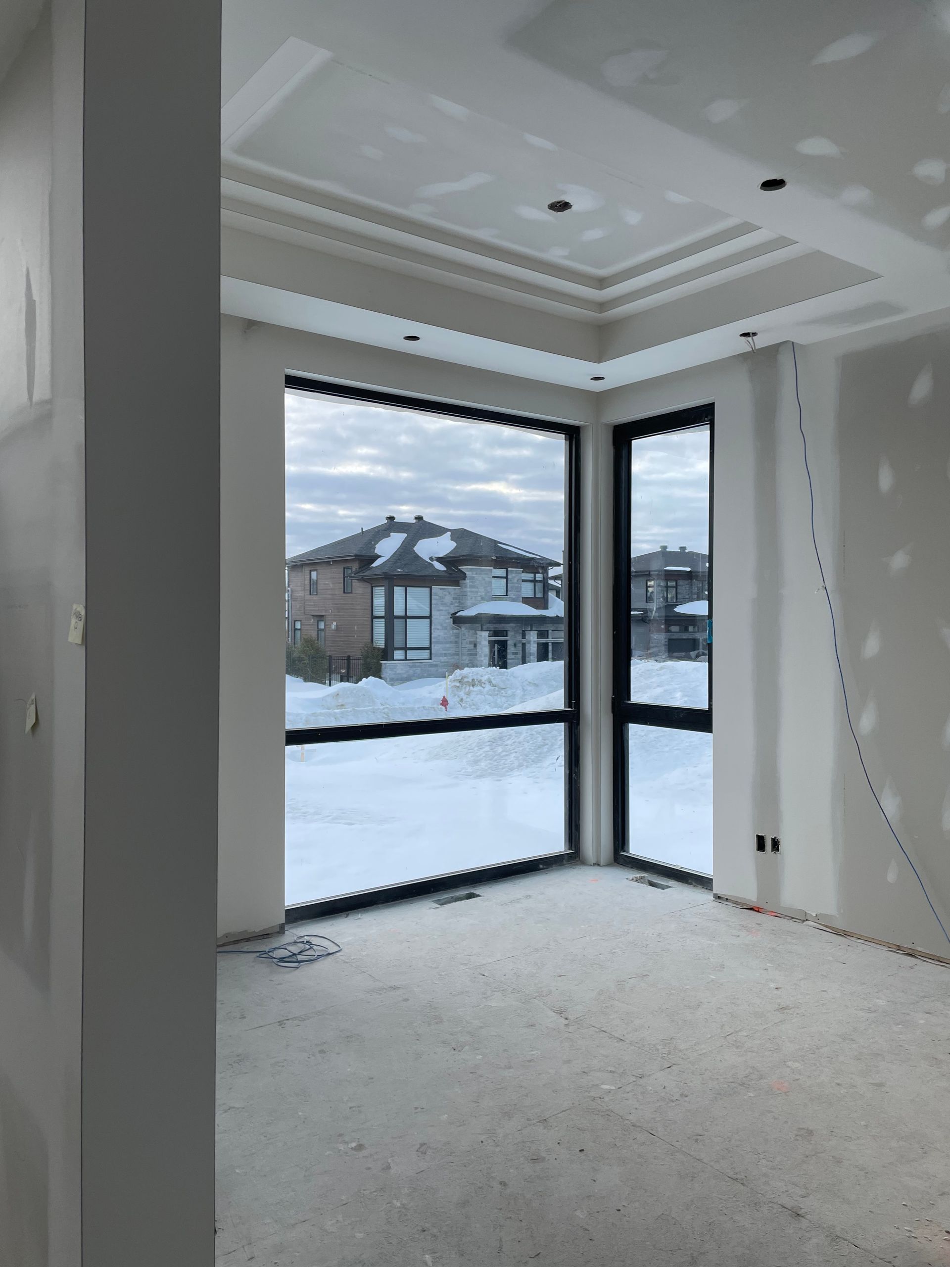 Intérieur d'une pièce en construction avec de grandes fenêtres donnant sur un paysage enneigé.