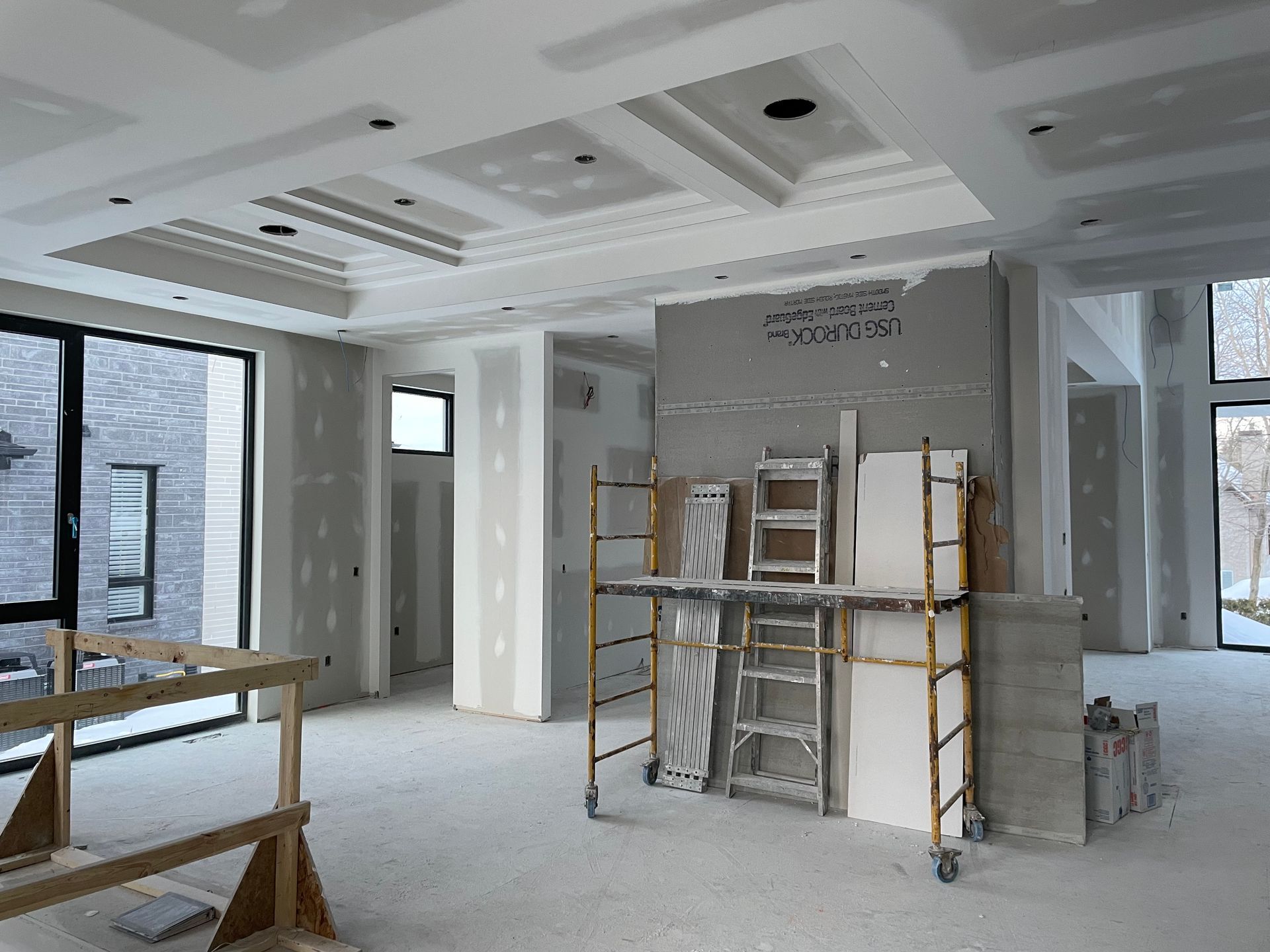 Intérieur d'une pièce en construction, avec cloisons sèches et échafaudages visibles, mettant en valeur un plafond à caissons.