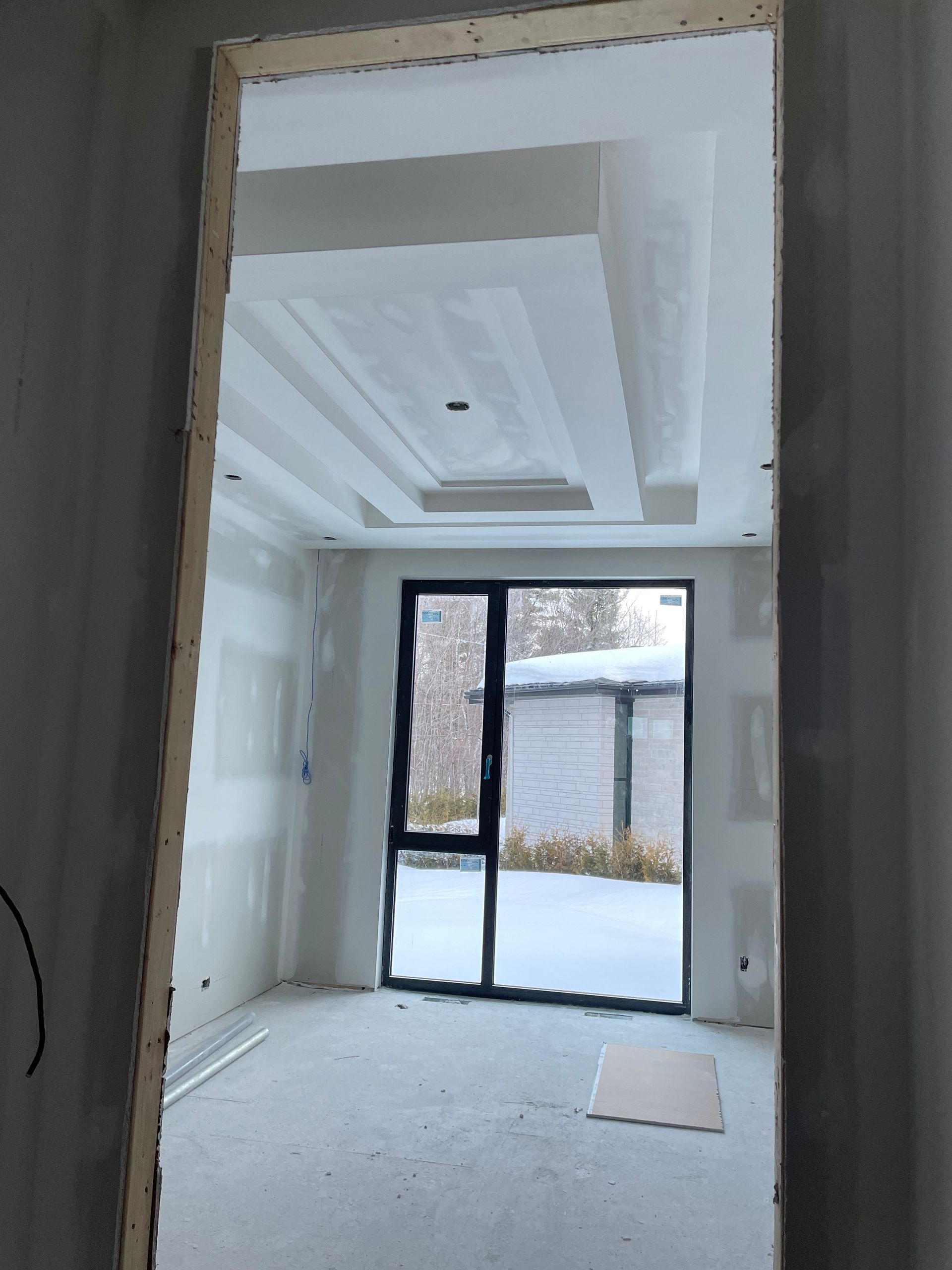 Vue intérieure d'une pièce en construction avec un plafond décoratif et une porte vitrée donnant sur un espace extérieur enneigé.