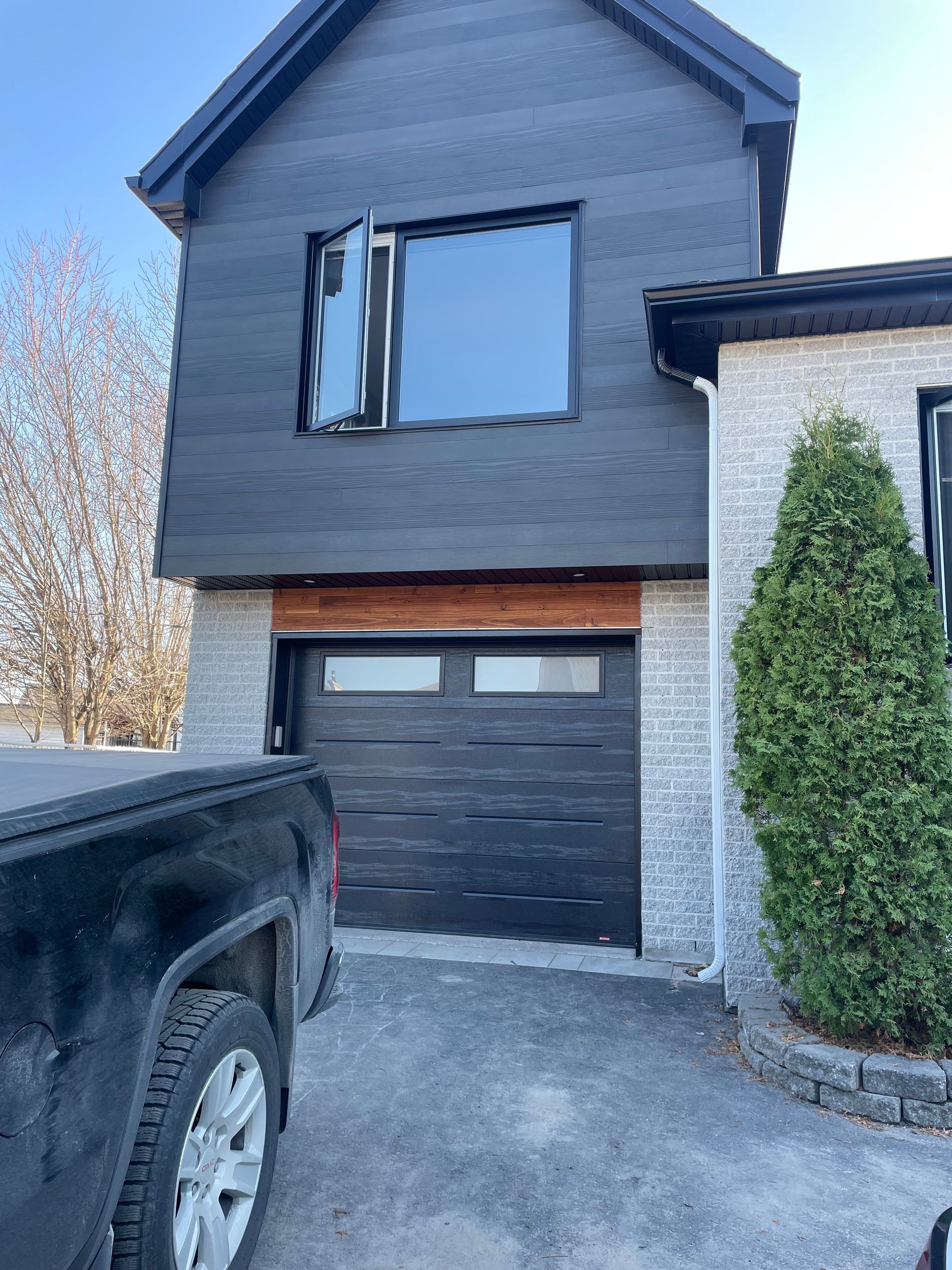 Maison aux murs noirs avec garage et fenêtre ouverte ; un camion est garé devant.