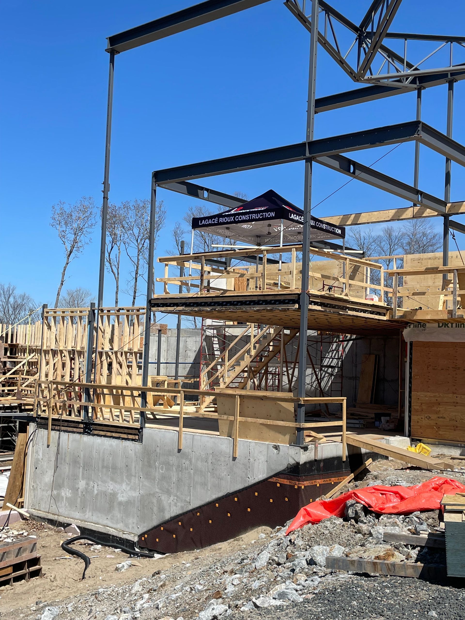 Chantier de construction avec charpente métallique et coffrage en bois se détachant sur un ciel bleu azur.