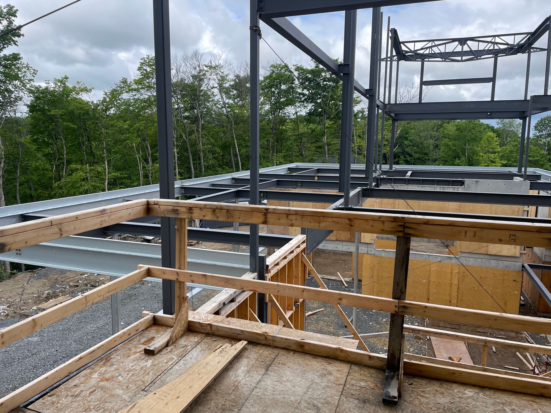 Chantier : Structure métallique d'un bâtiment avec rambarde de sécurité en bois. Arbres en arrière-plan.