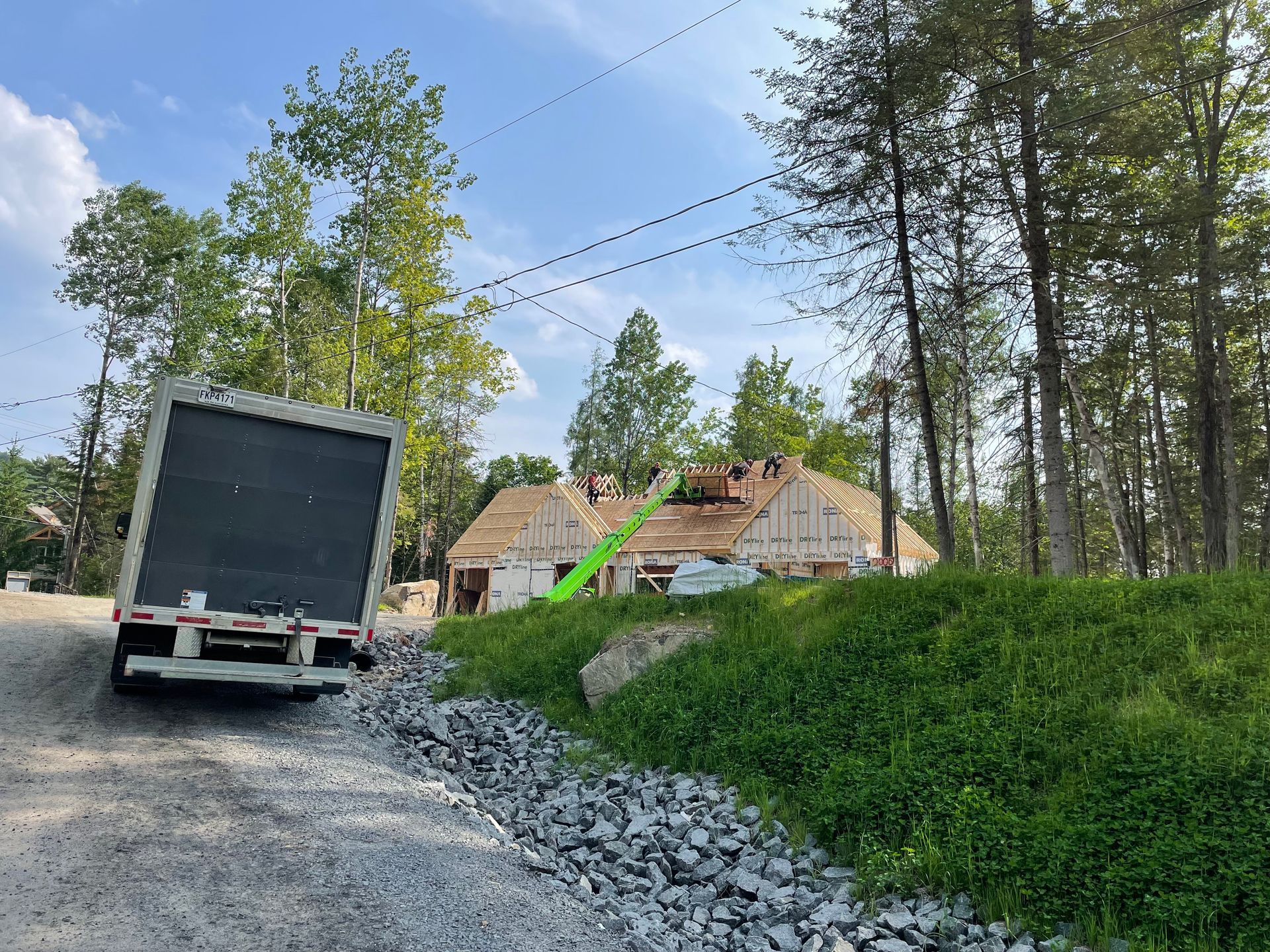 Camion stationné sur un chantier de construction, charpente de toit apparente, entouré d'arbres.