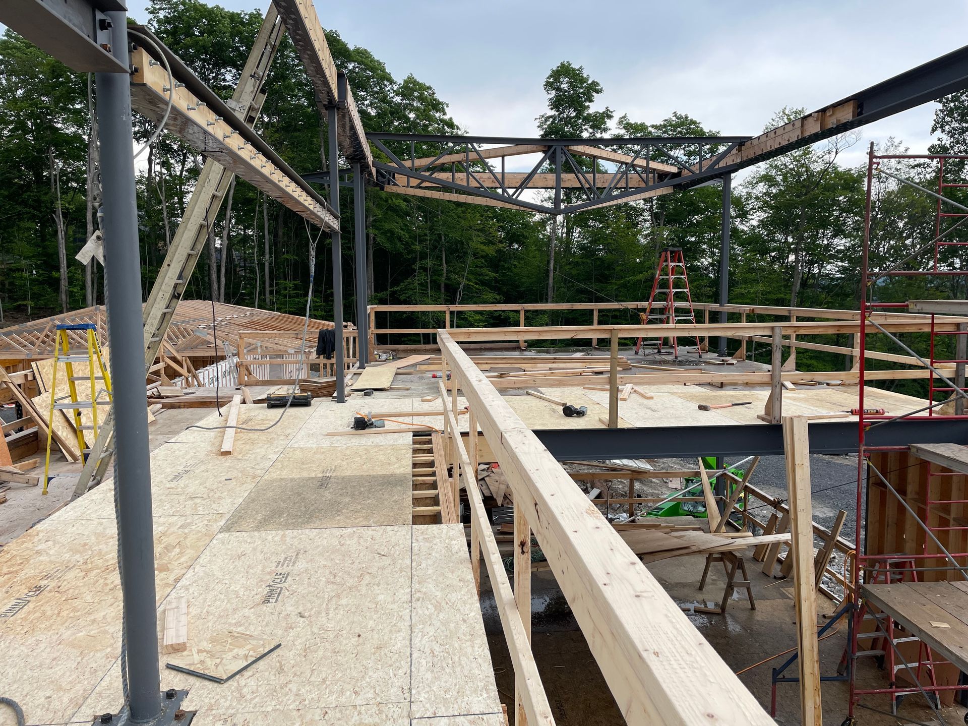 Chantier de construction avec poutres d'acier apparentes, platelage en bois et garde-corps de sécurité ; environnement extérieur.