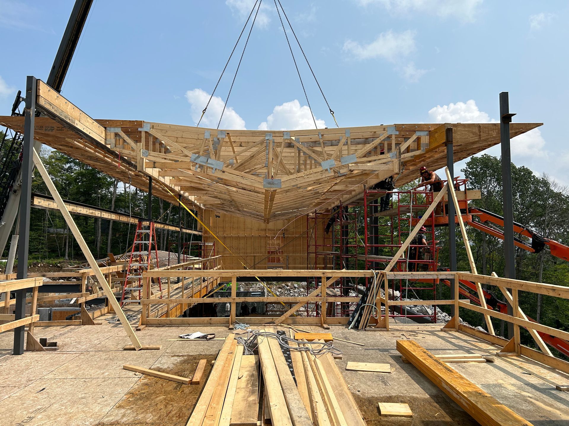 Chantier de construction où une charpente de toit en bois est mise en place par une grue.
