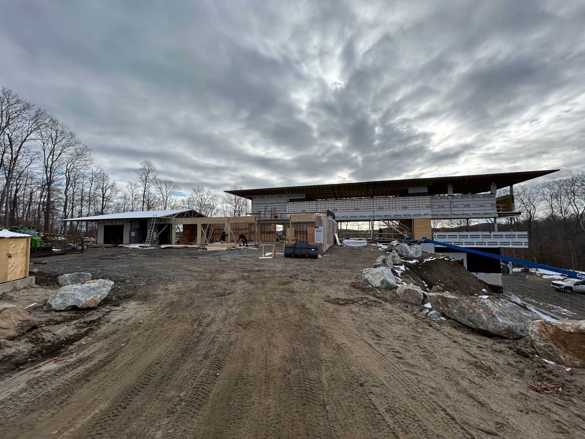 Chantier de construction avec structure de bâtiment, chemin de terre, ciel nuageux.