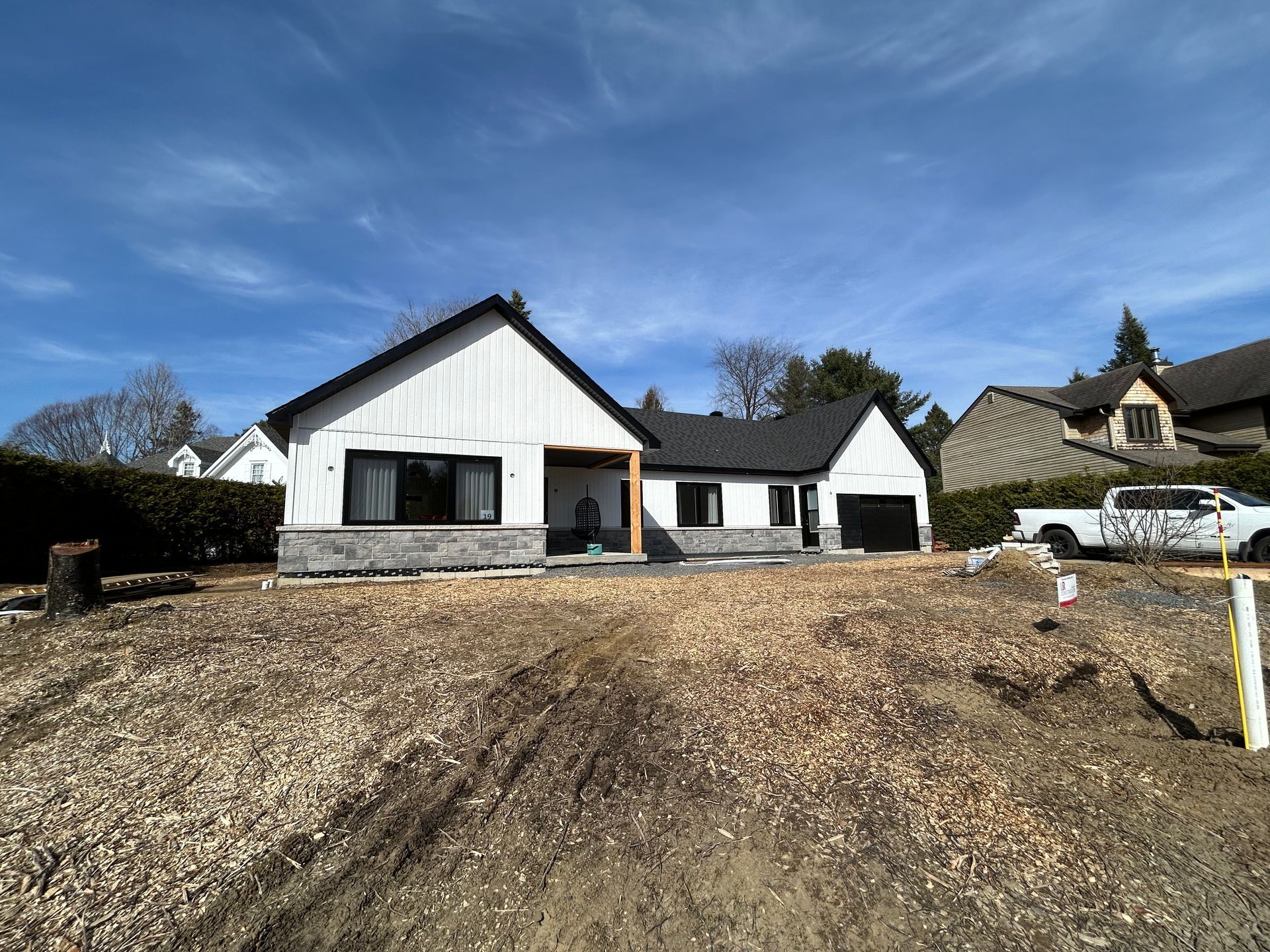 Maison neuve avec bardage blanc, toit noir et façade en pierre, sous un ciel bleu.
