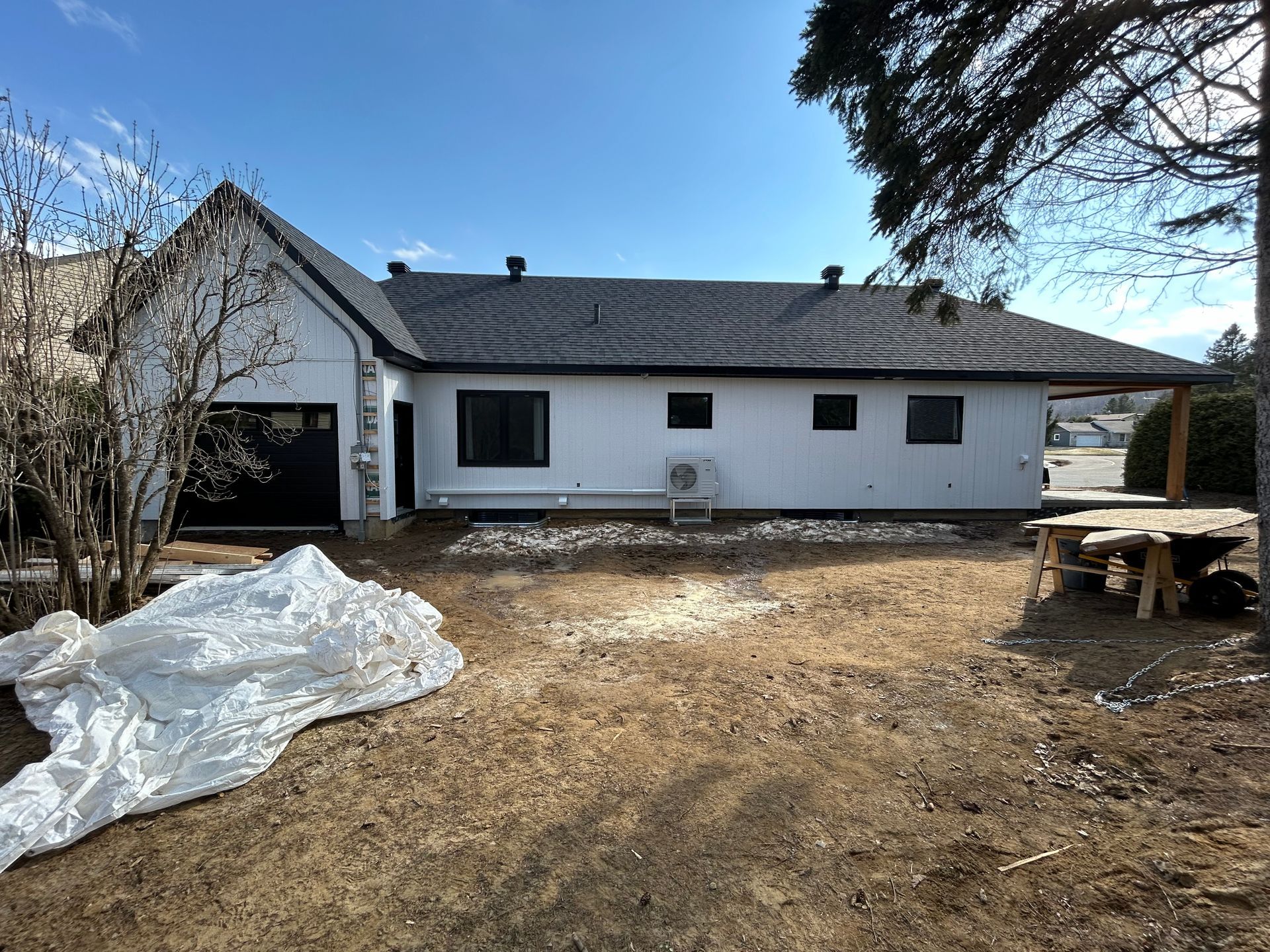 Maison blanche aux fenêtres et au toit noirs, située dans une cour sous un ciel dégagé.