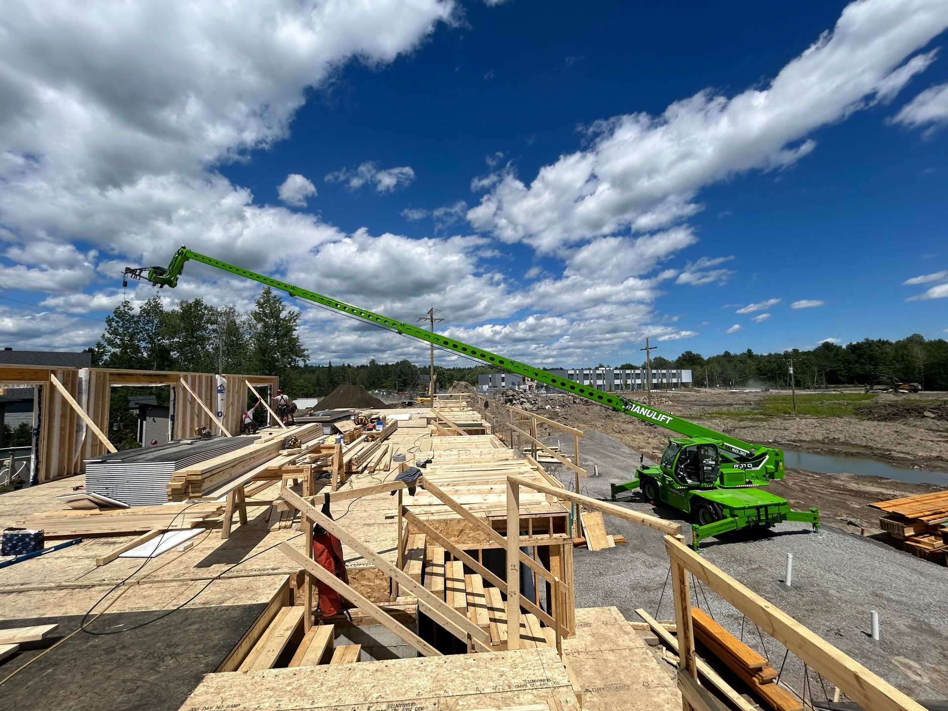 Chantier de construction avec ascenseur vert, charpente en bois et ciel bleu.
