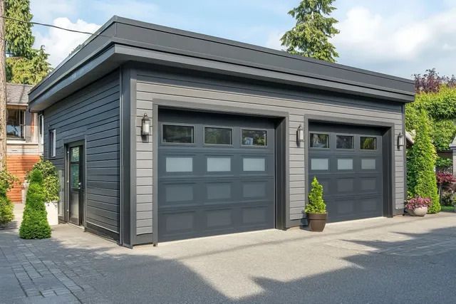 Garage gris moderne avec deux portes noires et une allée devant