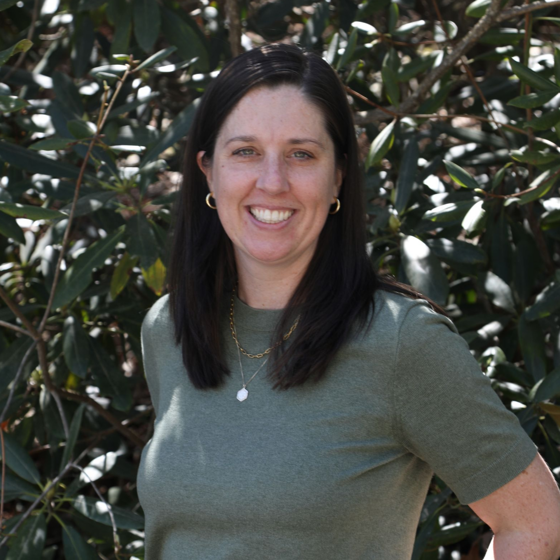Headshot of a person with shoulder-length brown hair, wearing a black blazer, smiling against a white background.